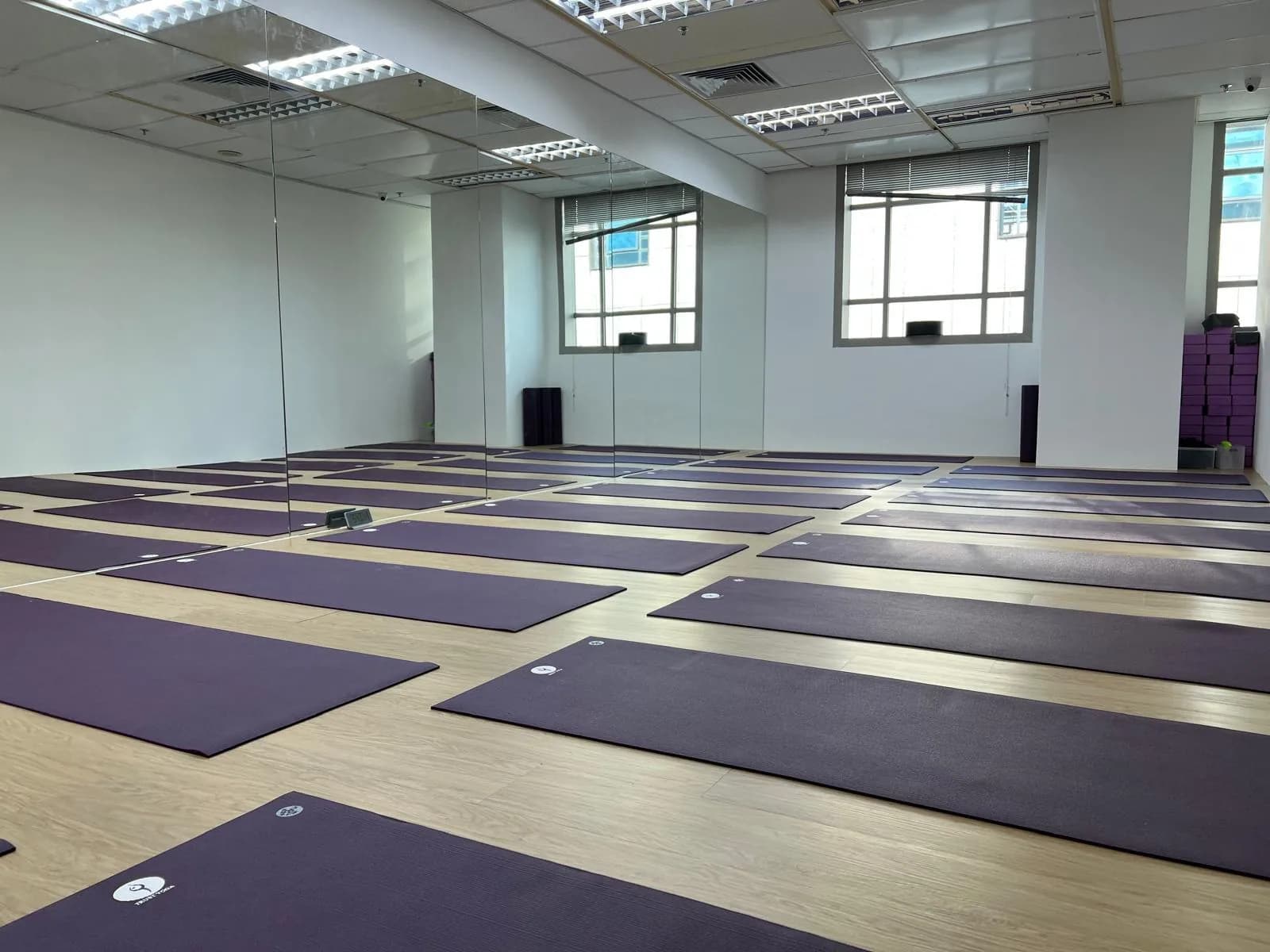 Yoga studio with purple mats laid out on wooden floor, mirror wall, and bright lighting