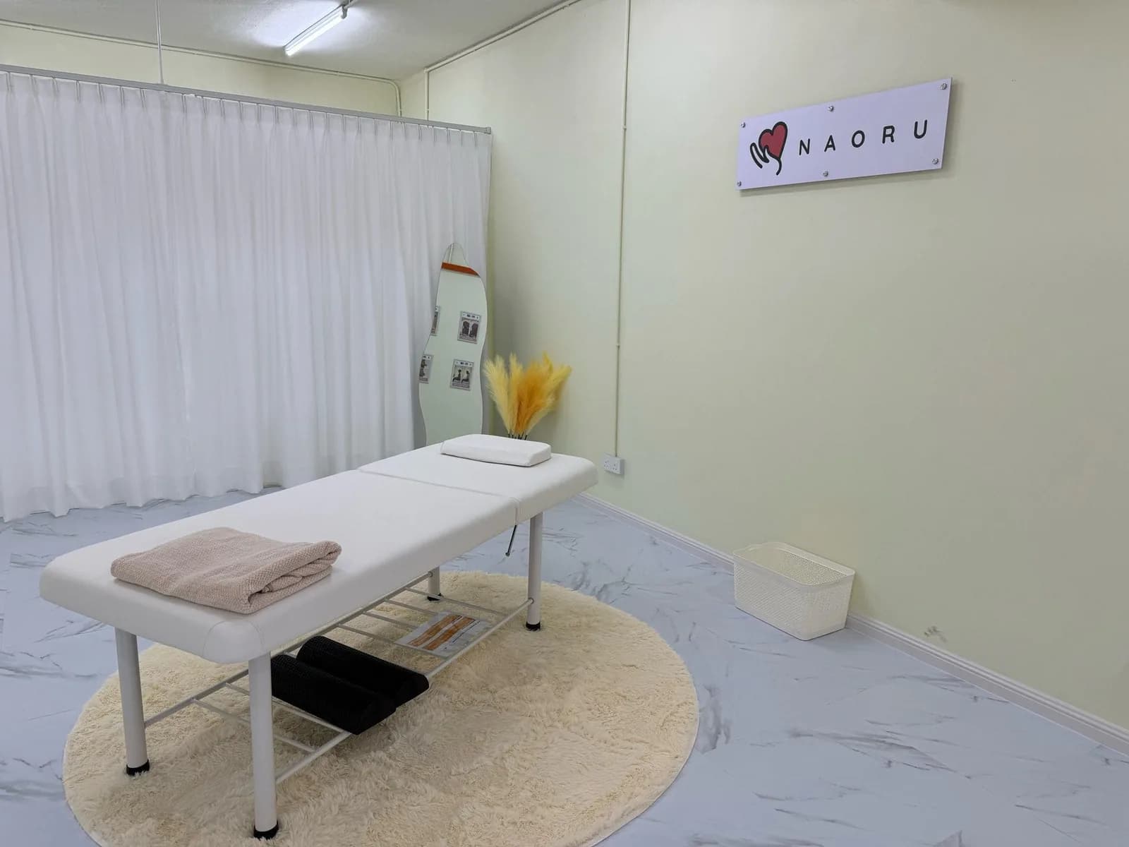 Clean treatment room with massage table, white curtain, and NAORU signage