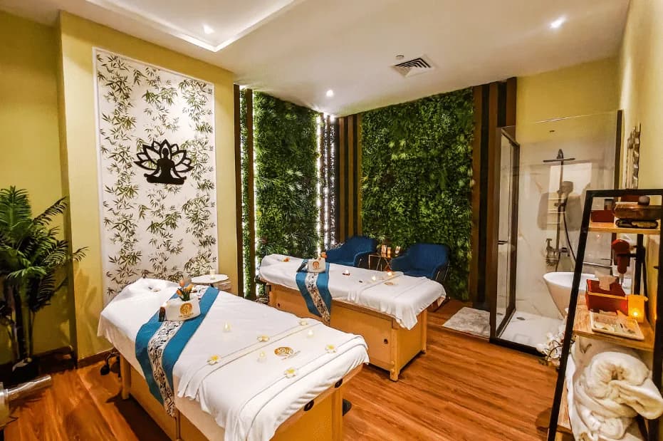 Spa treatment room with two massage beds, green plant walls, and lotus artwork decor