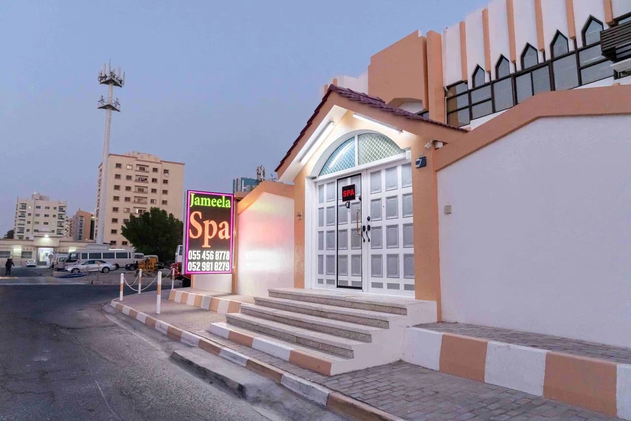 Jameela Spa storefront in Ajman with peach-colored building, white doors, and illuminated signage at dusk
