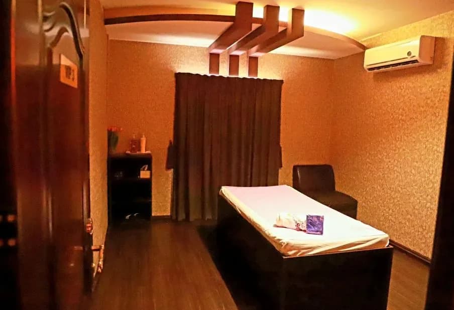 Massage room with treatment bed, orange walls, and wooden ceiling fixtures