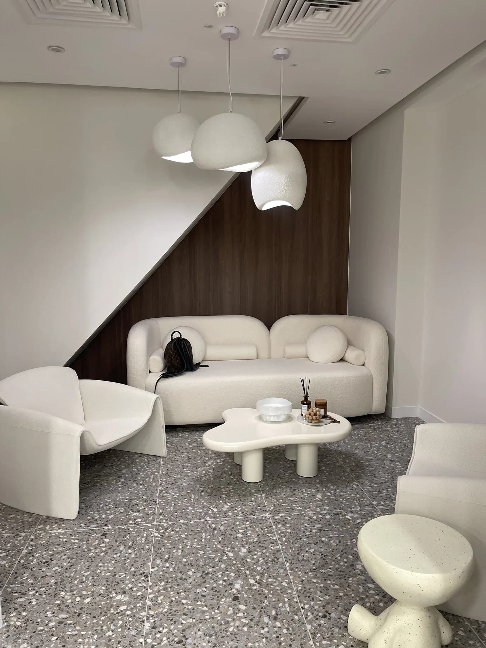 Modern salon waiting lounge with cream curved seating, white pendant lights, and decorative floor