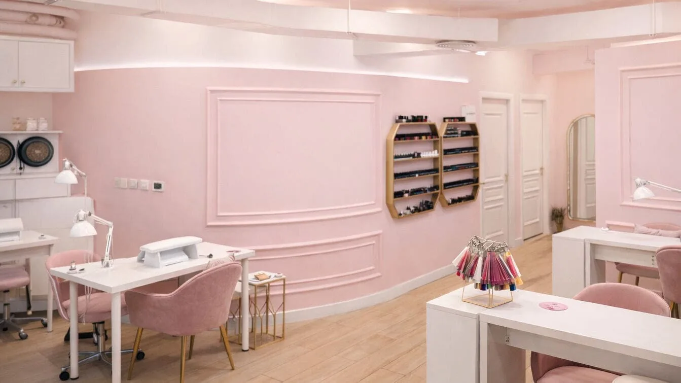 Modern salon interior with pink walls, white workstations, and product displays