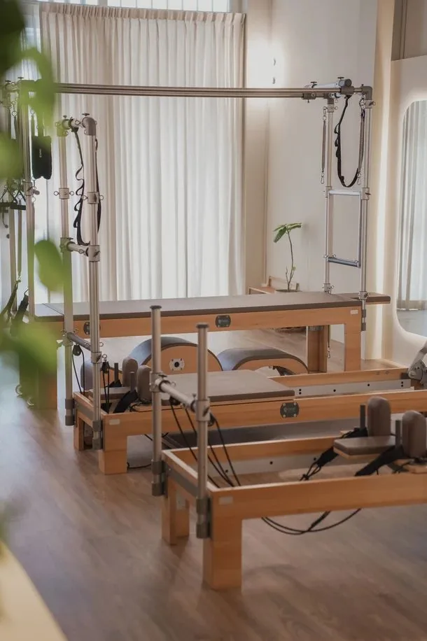 Pilates reformer machines in a bright studio with large windows and wooden floors