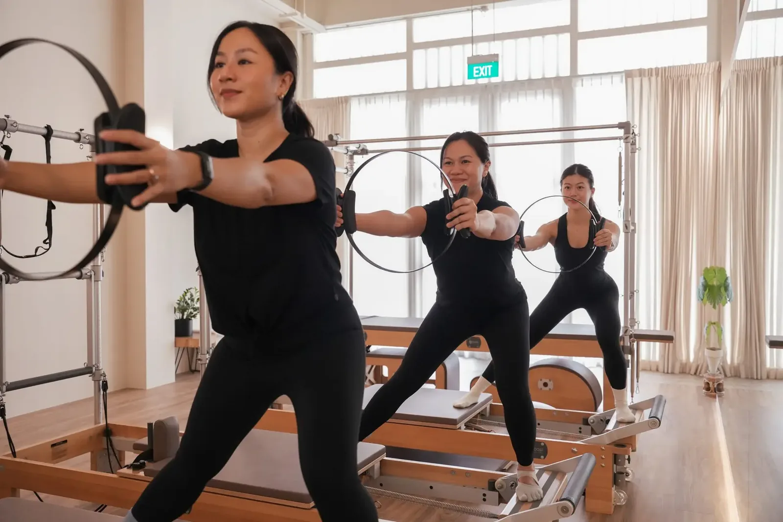 Pilates instructor and students using resistance rings on reformers in a bright studio