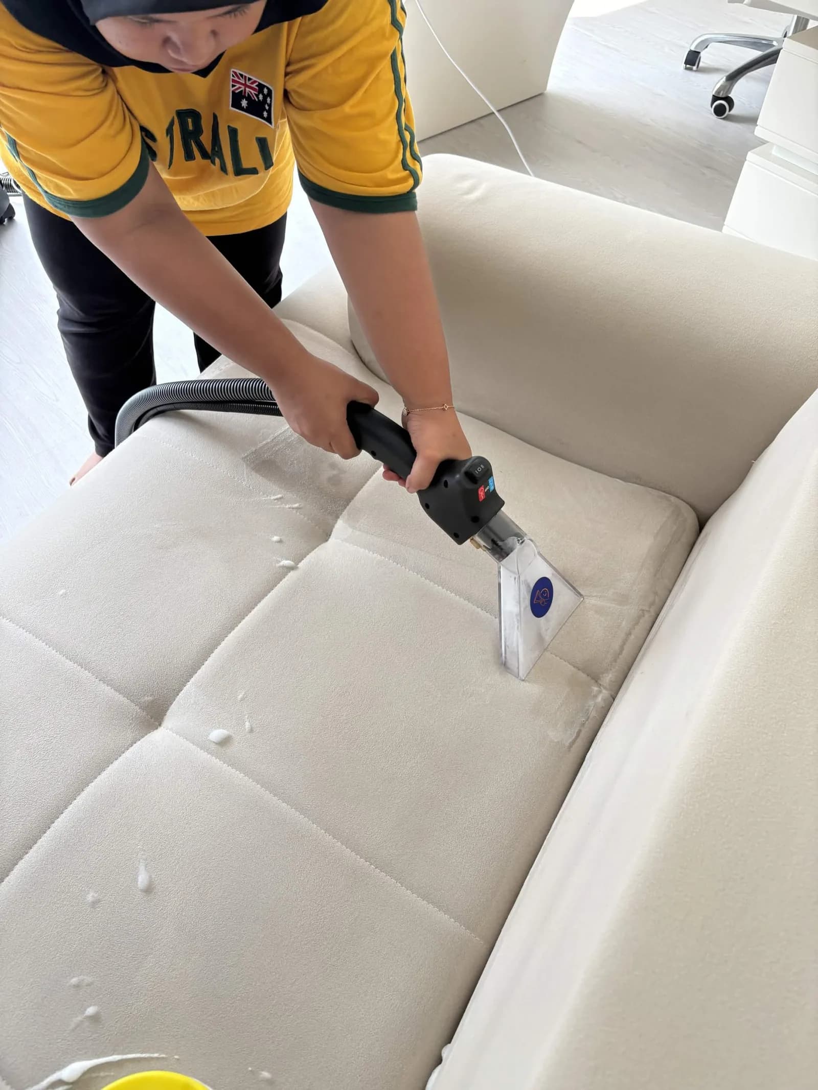 Worker cleaning upholstered sofa with extraction equipment