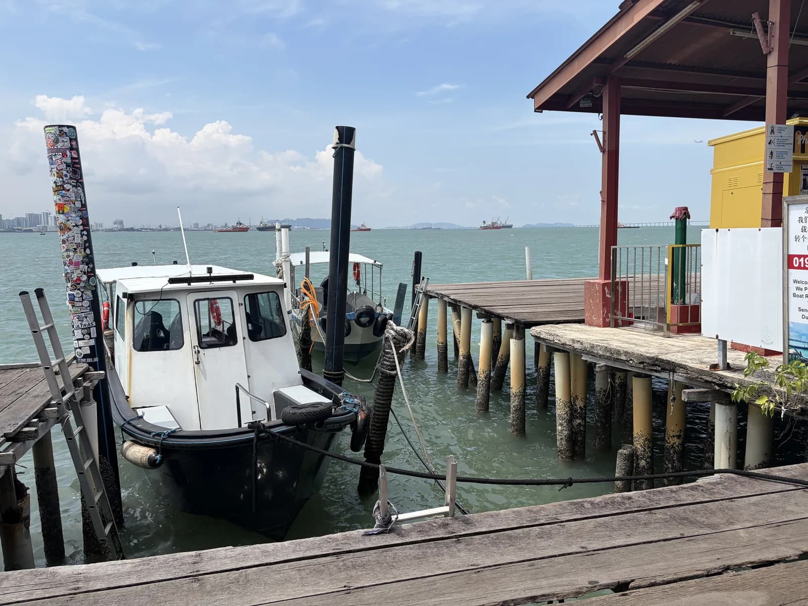 White fishing boat moored at traditional wooden jetty with stilt structures over water and covered shelter.