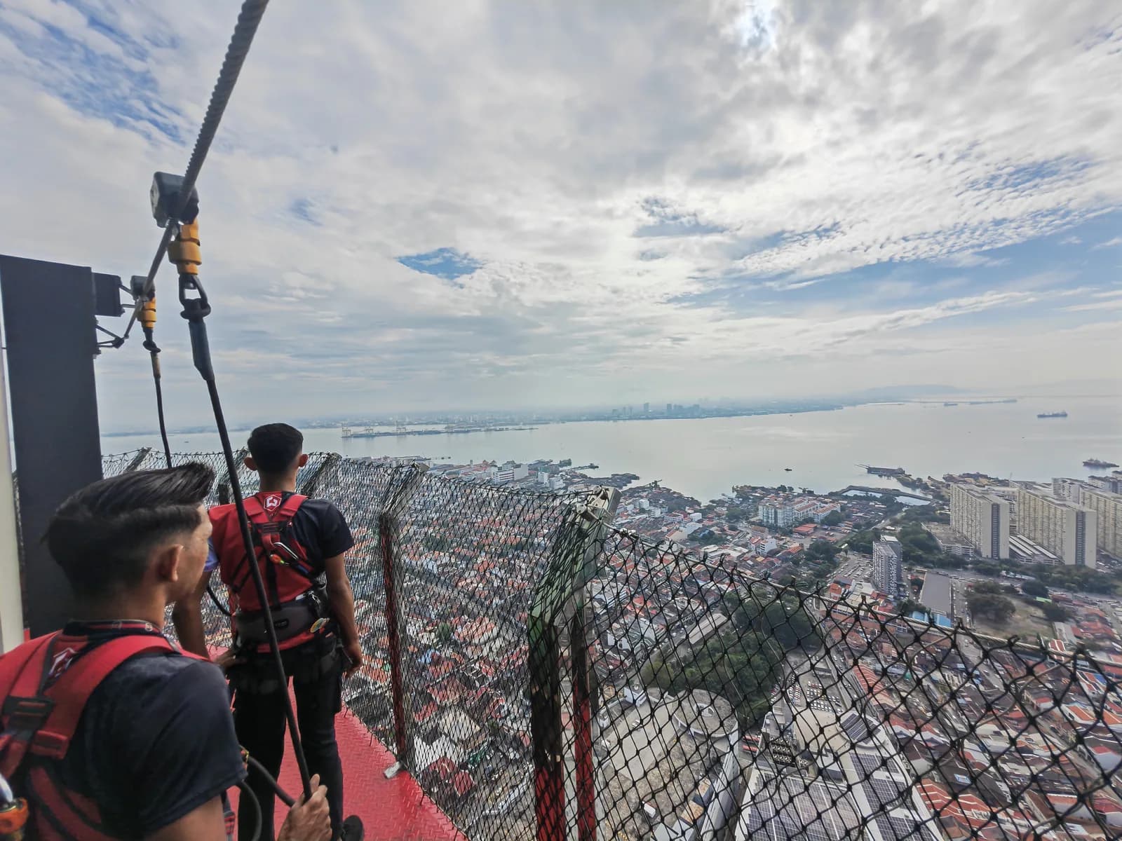 Visitors harnessed on Rainbow Skywalk platform overlooking coastal city and bay below