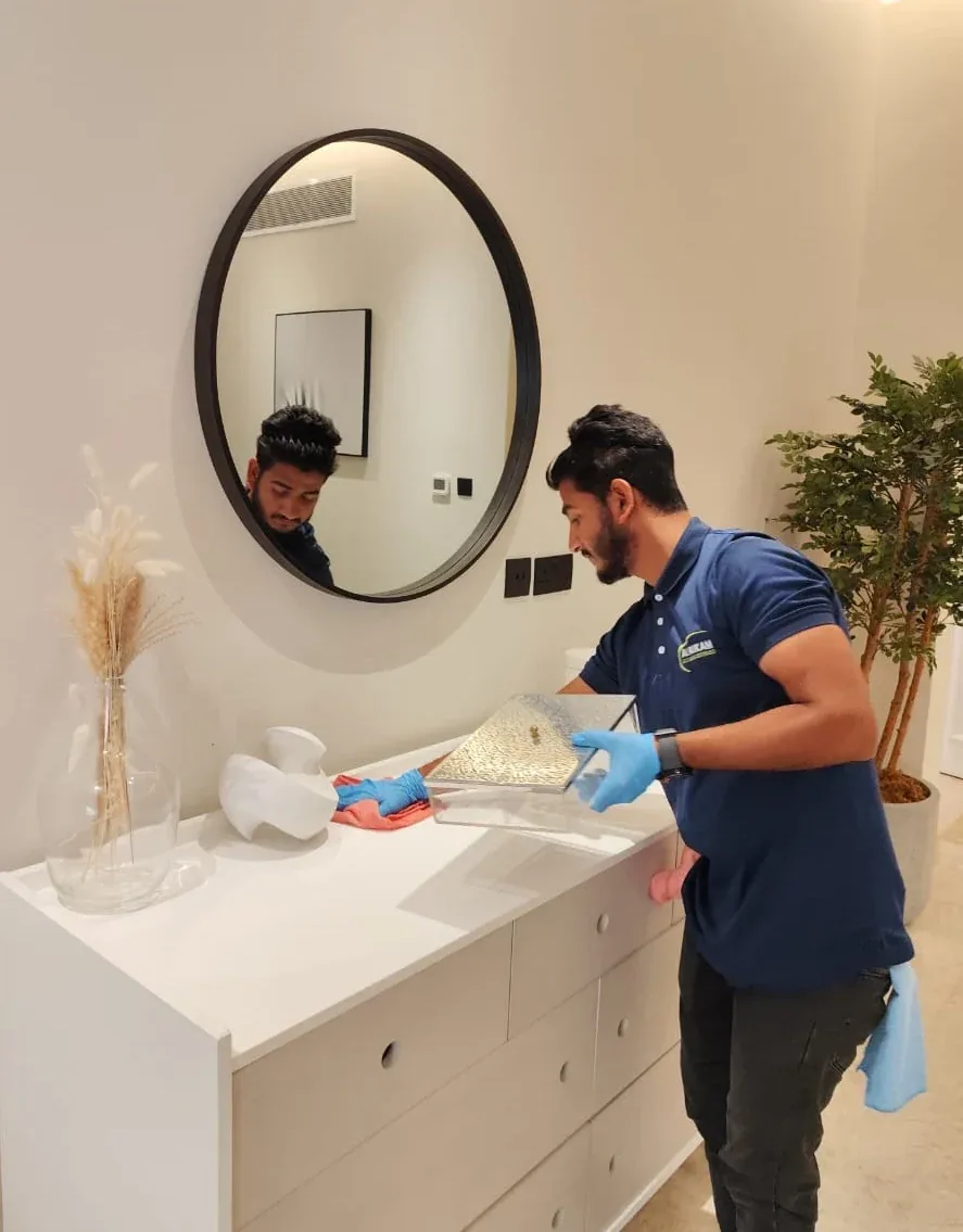 Cleaning worker in blue uniform cleaning a bathroom sink and counter with professional supplies