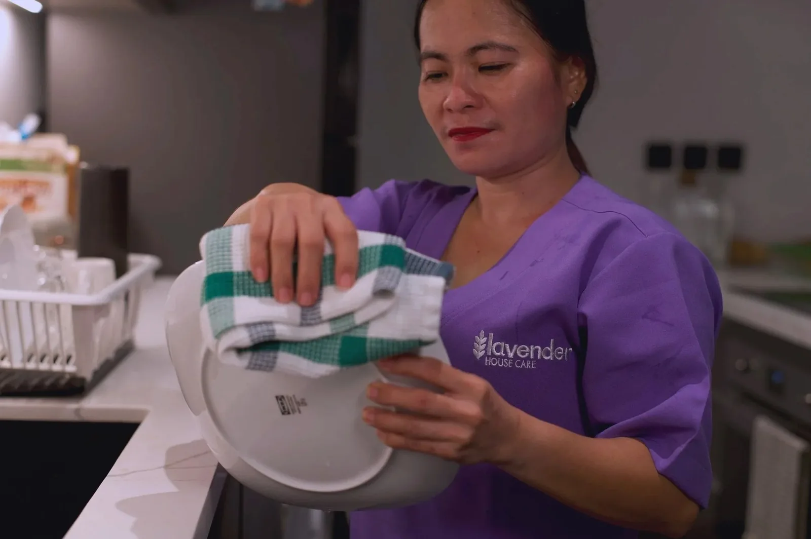Staff member in purple uniform folding a striped towel in a bright kitchen space