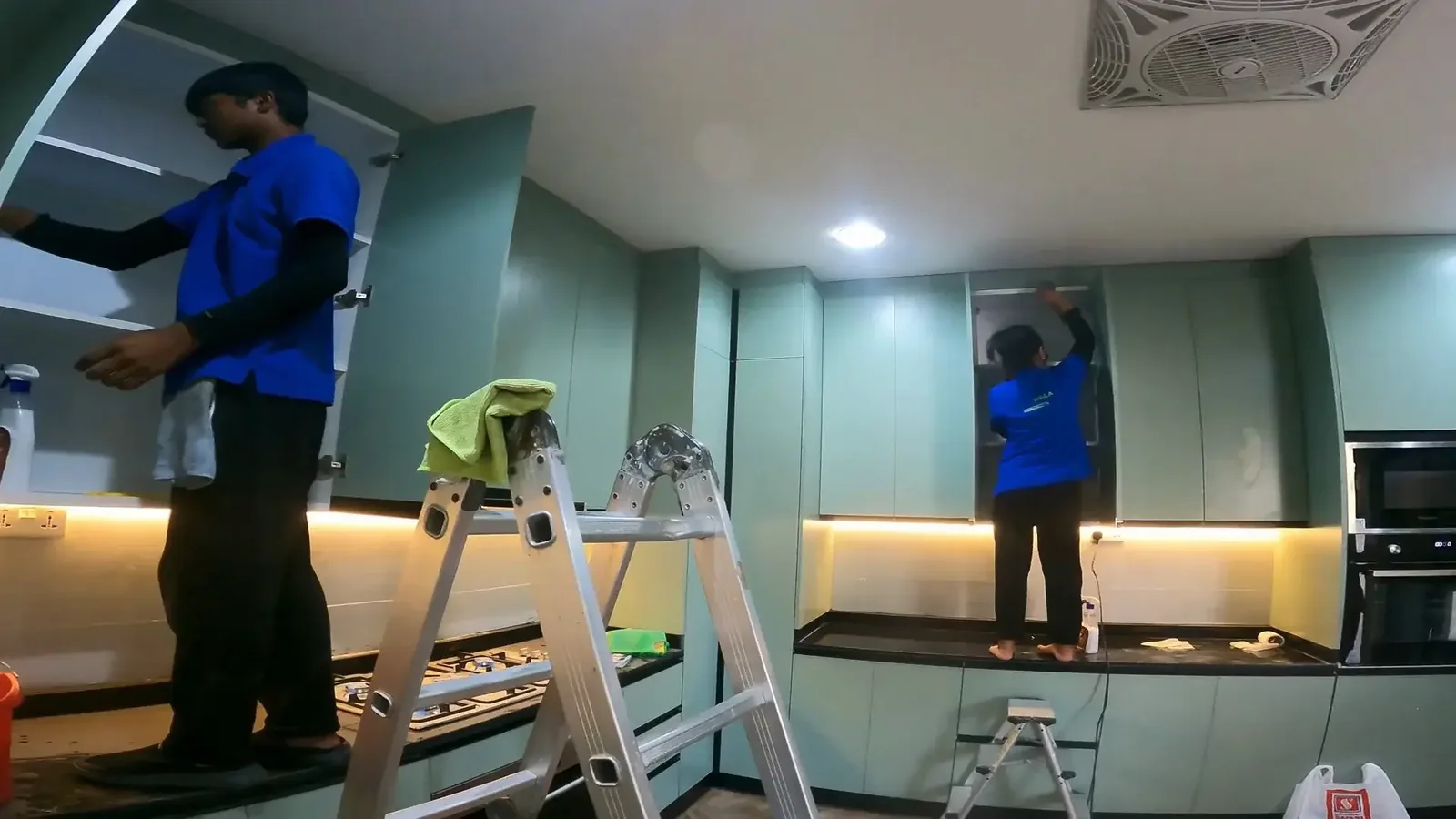 Team members installing or cleaning modern kitchen with mint green cabinets and lighting
