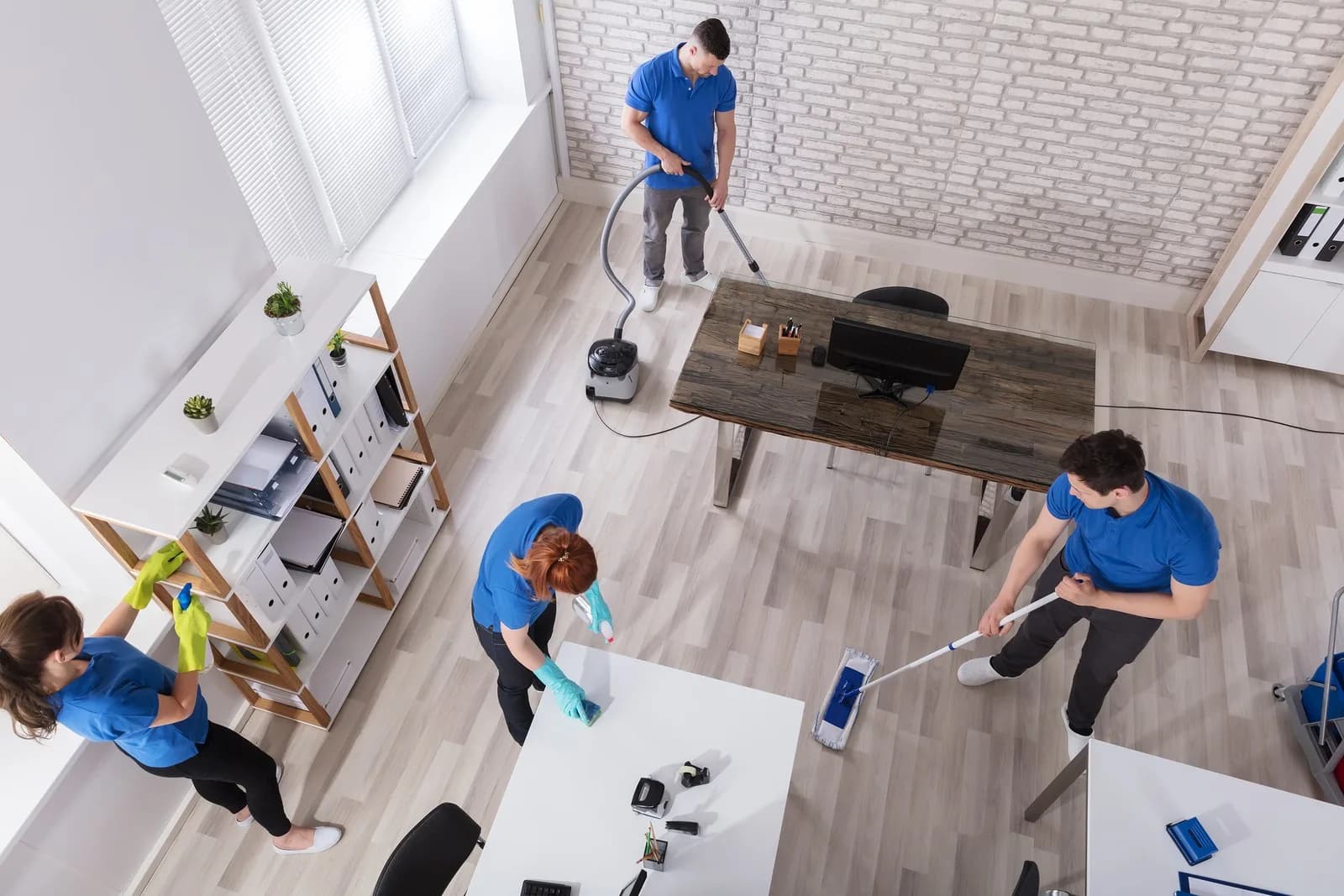 Cleaning team in blue uniforms working in a bright office space with cleaning equipment