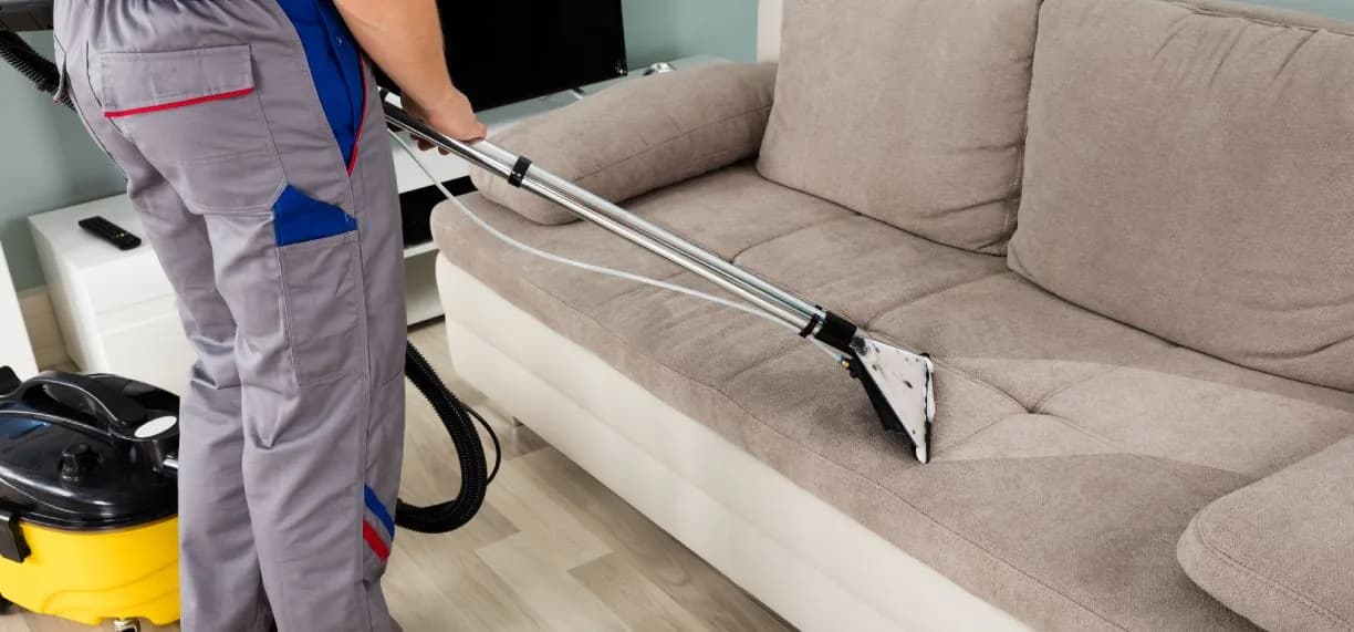 Cleaner using professional equipment to deep clean a beige sofa