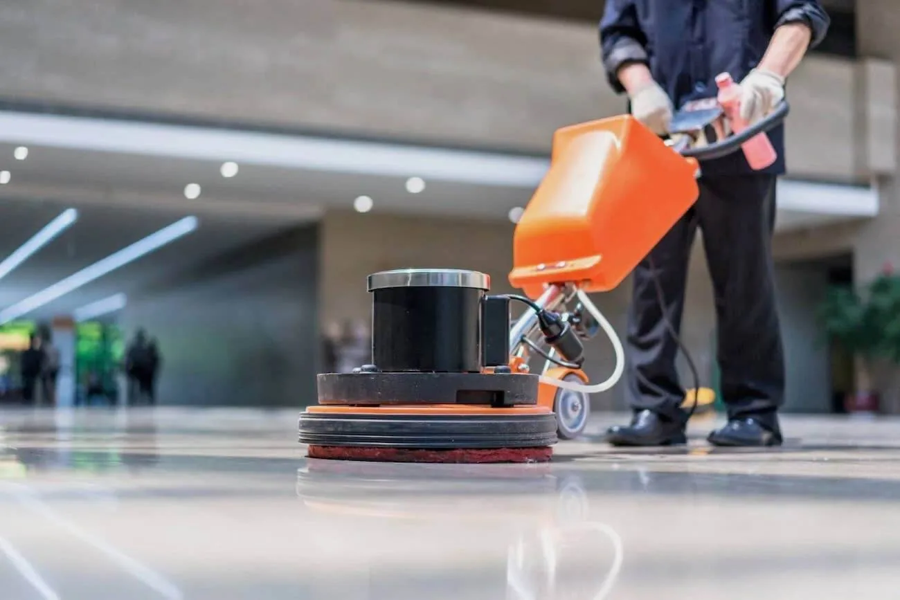 Worker using an orange floor buffer machine on a shiny polished floor