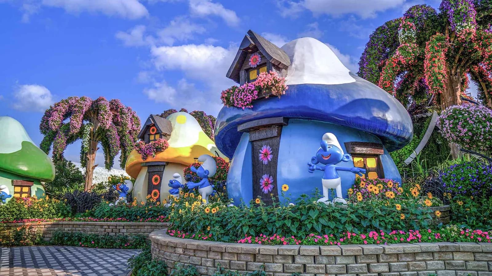 Blue and yellow mushroom-shaped garden structures with flowering vines and colorful flower beds