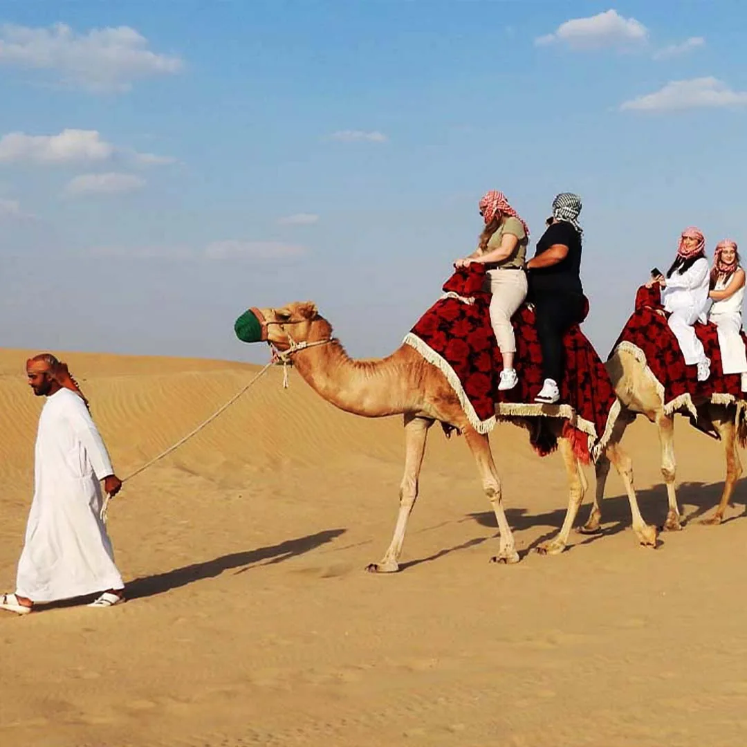 Camel ride tour in the desert with guide leading tourists across golden sand dunes