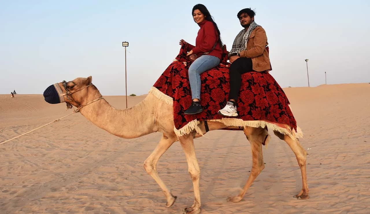 Tourists on camel ride across sandy desert landscape with dunes and sky.