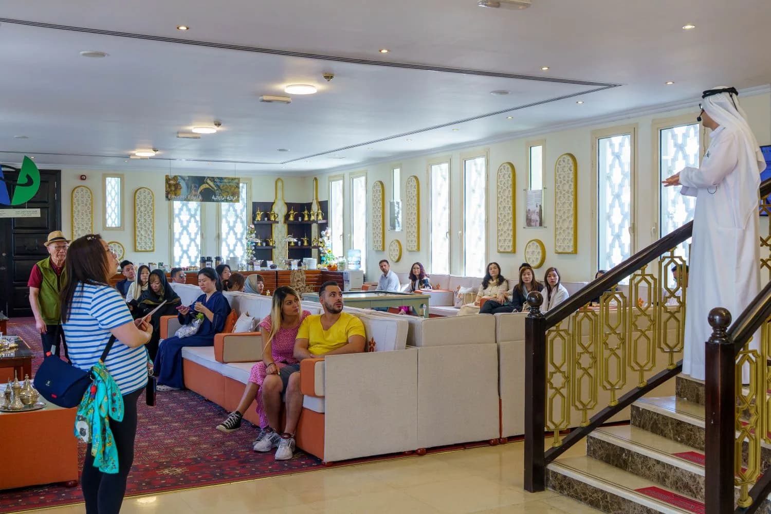 Prayer hall interior with beige seating, gold window frames, and tour group of visitors
