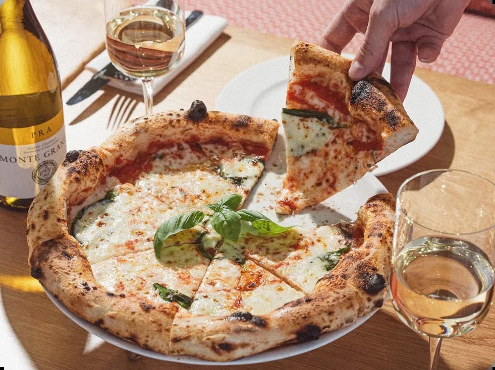 Pizza with melted cheese and basil leaf, wine bottle and glasses on wooden table