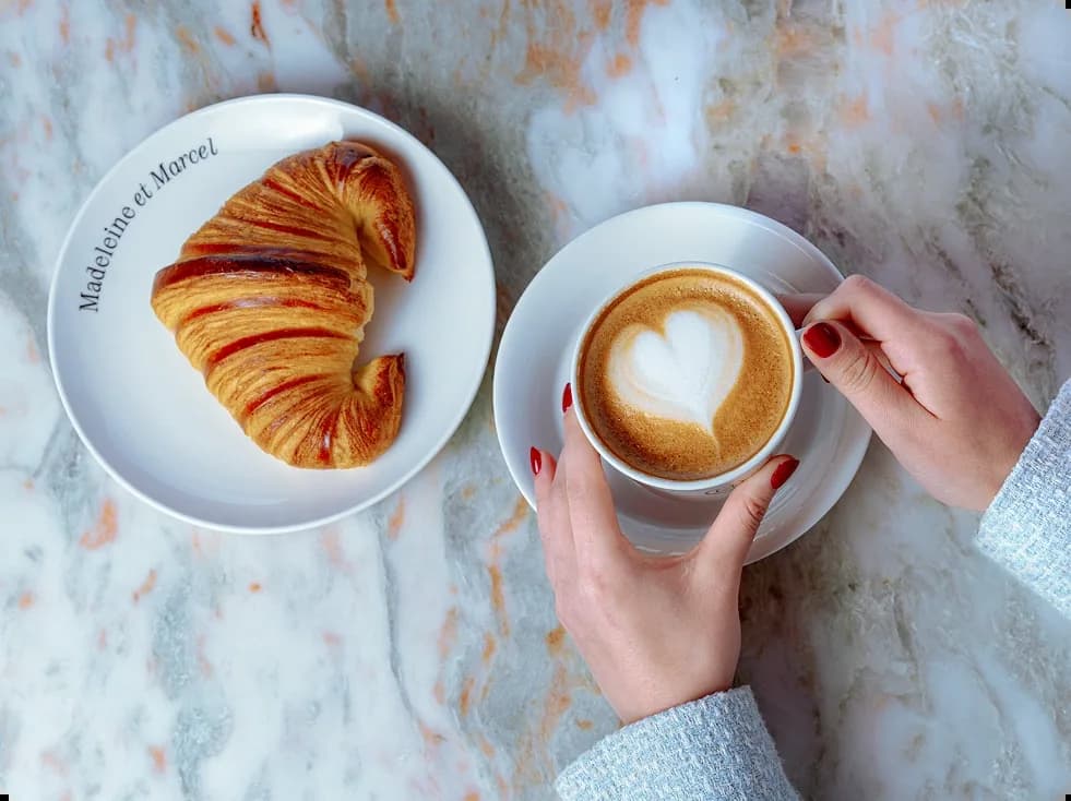 Cappuccino with heart latte art and jam-filled croissant on marble table