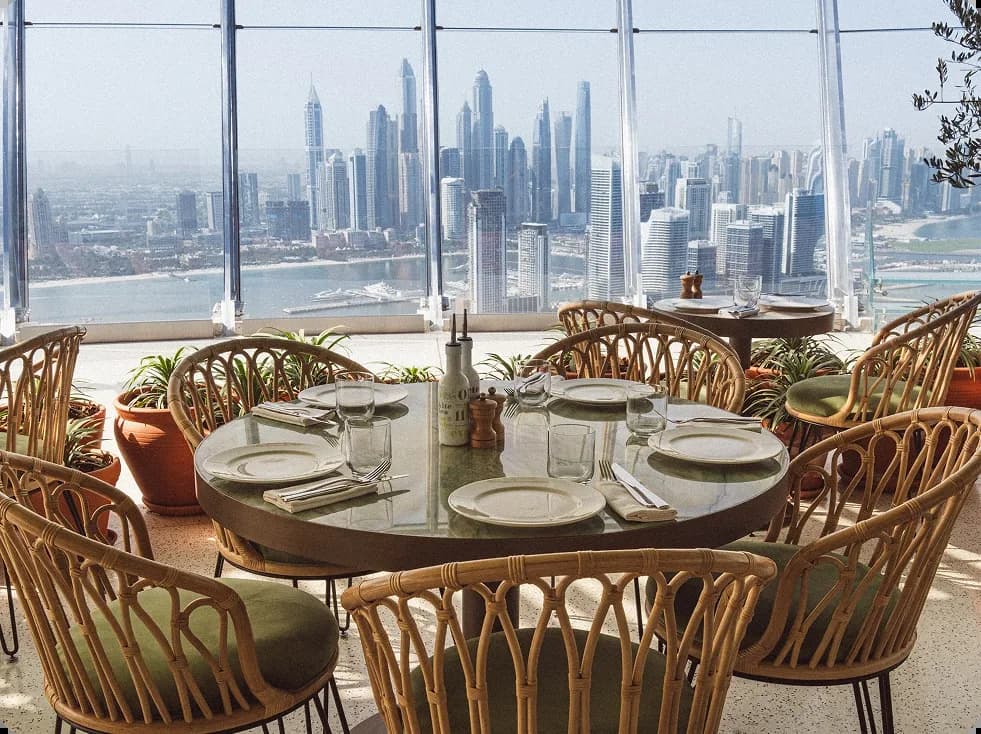 Fine dining table set with place settings and wine, overlooking city skyline through expansive windows.