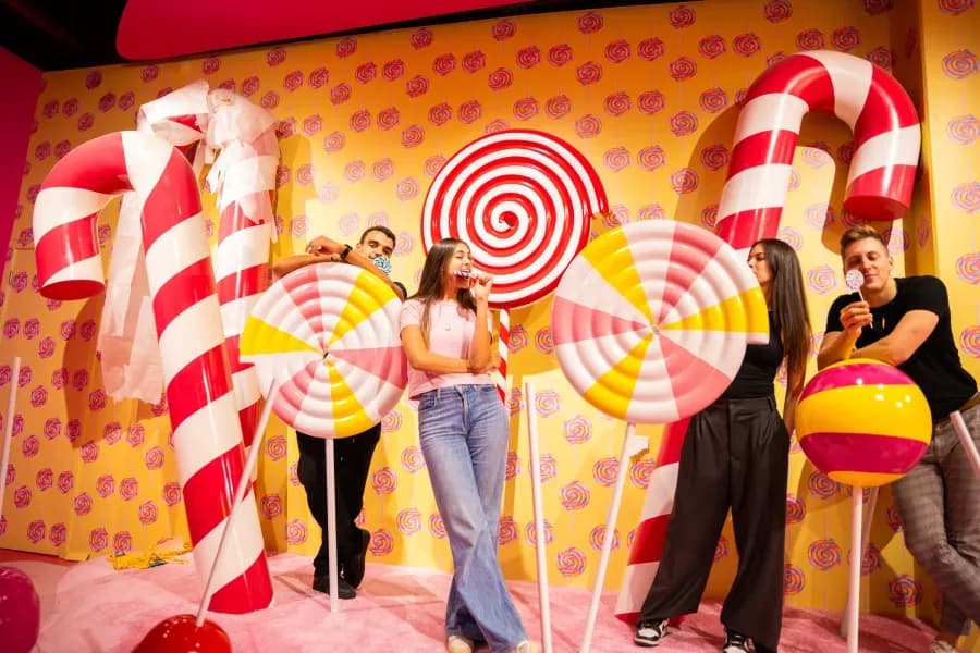 Candy museum interior with giant lollipops, candy canes, and colorful wall decorations with visitors
