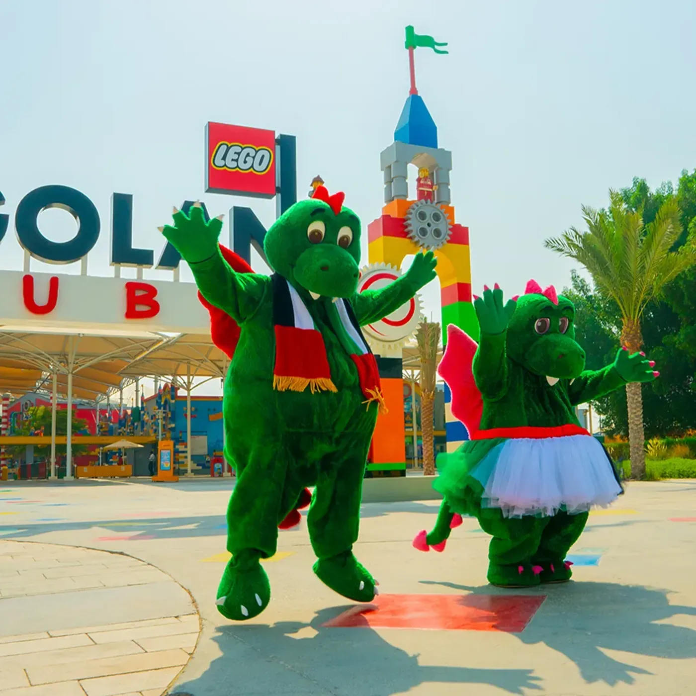 LEGO character mascots posing at LEGOLAND Dubai entrance with castle tower behind