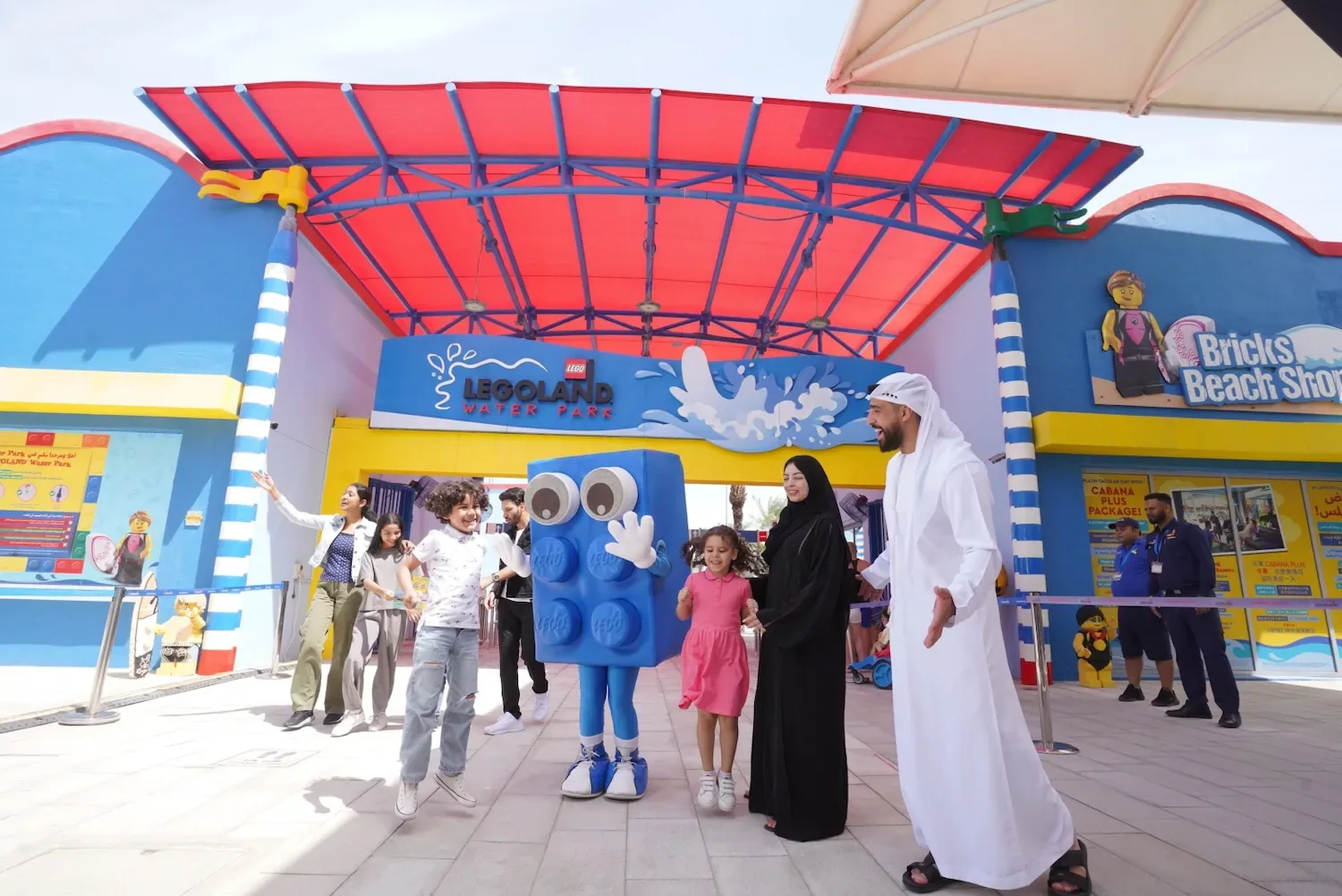 Legoland Dubai entrance with LEGO brick mascot, colorful building facade, and visitors in plaza