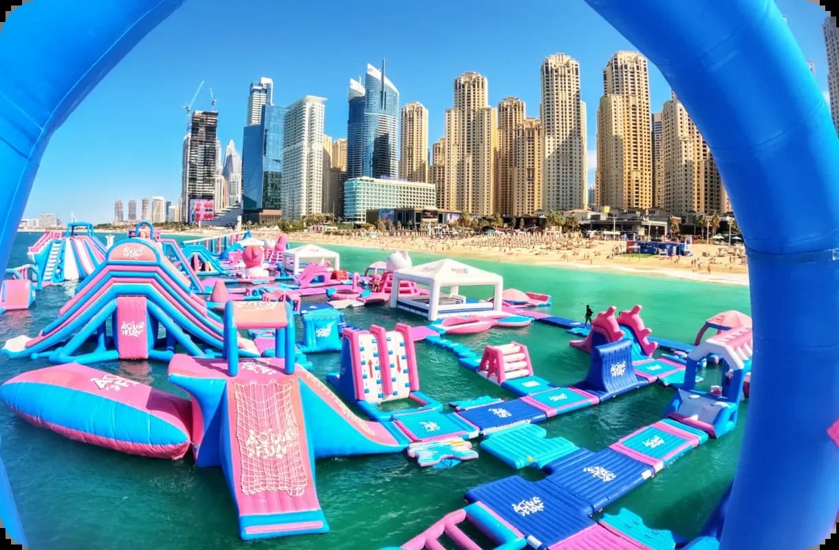 Inflatable water park with pink and blue obstacles on water, Dubai skyline behind