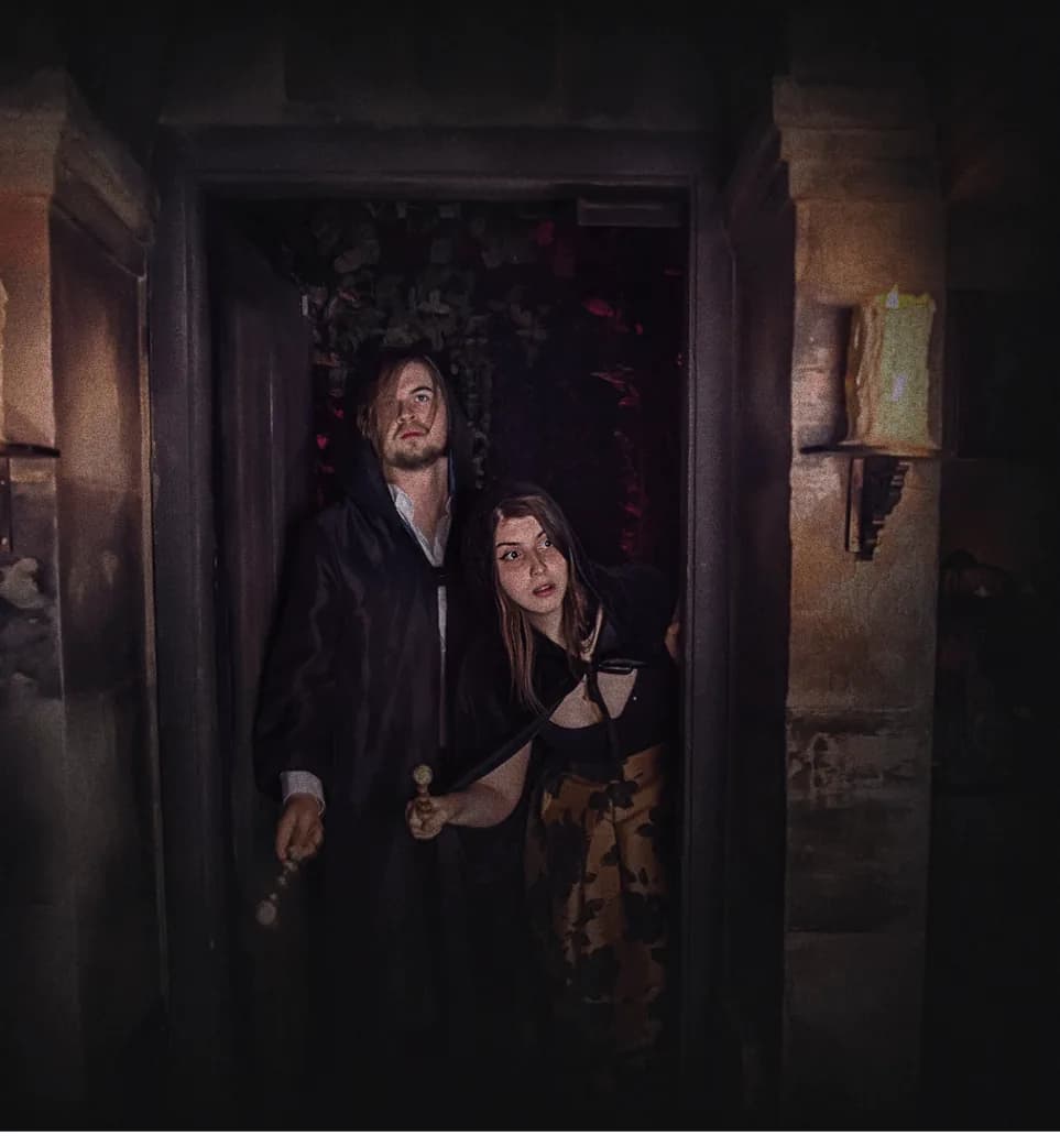 Visitors in a dark dungeon-themed escape room with stone walls and red atmospheric lighting