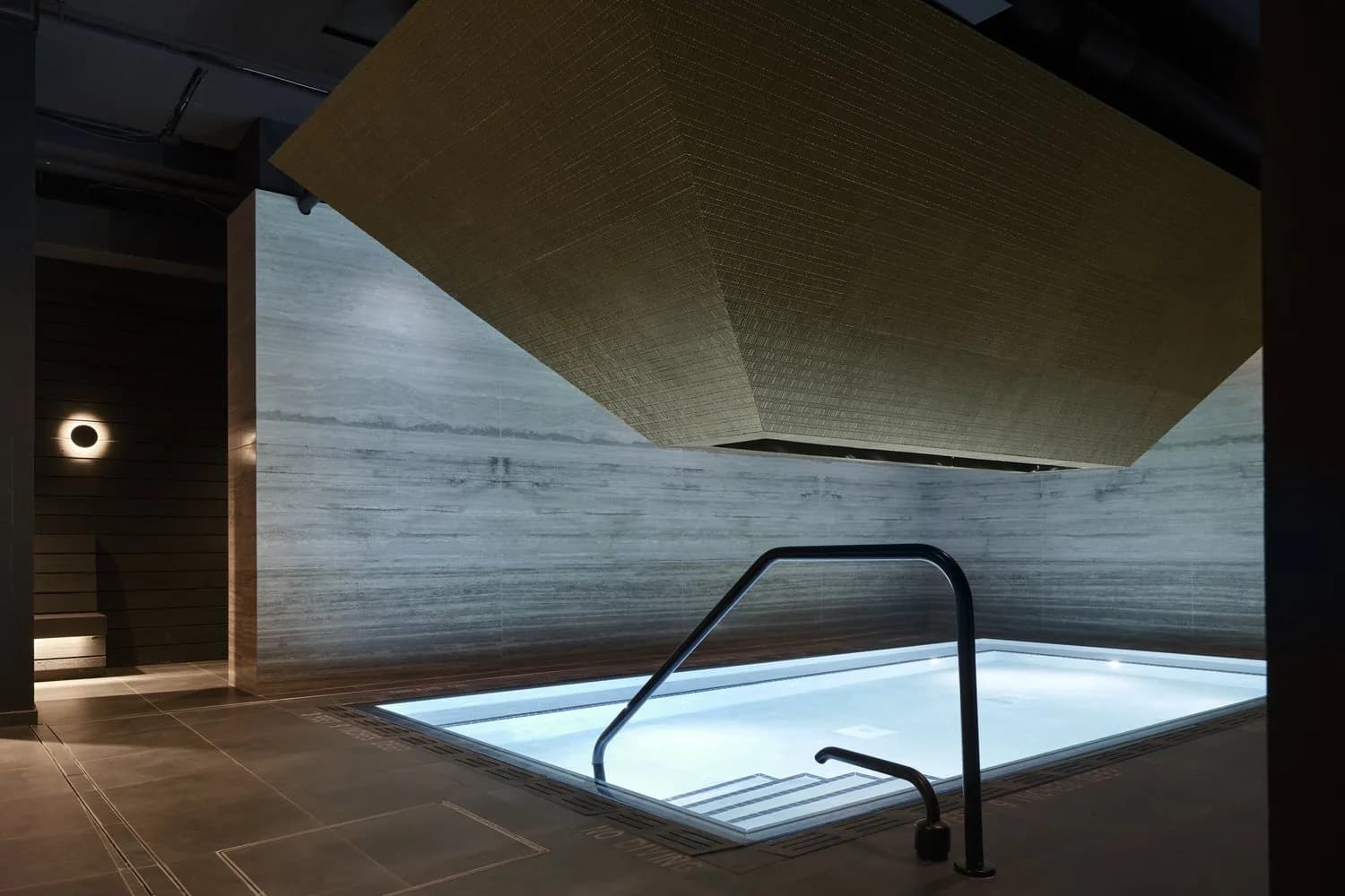 Modern bathhouse interior with rectangular soaking tub, geometric ceiling, and ambient lighting