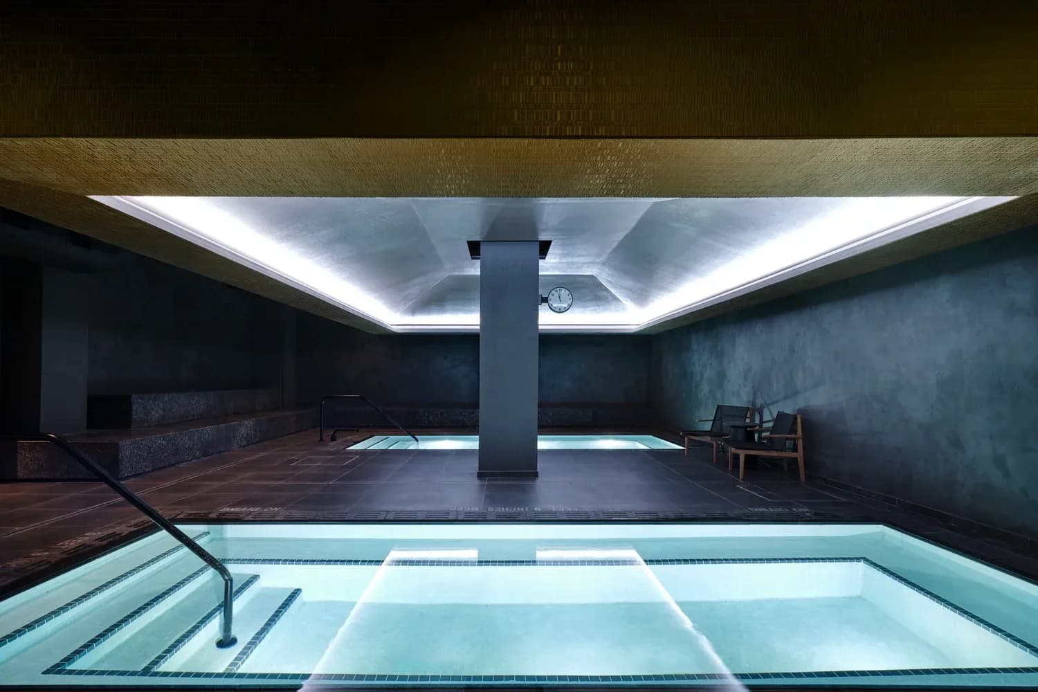 Modern bathhouse with multiple illuminated pools, dark walls, and contemporary lighting design