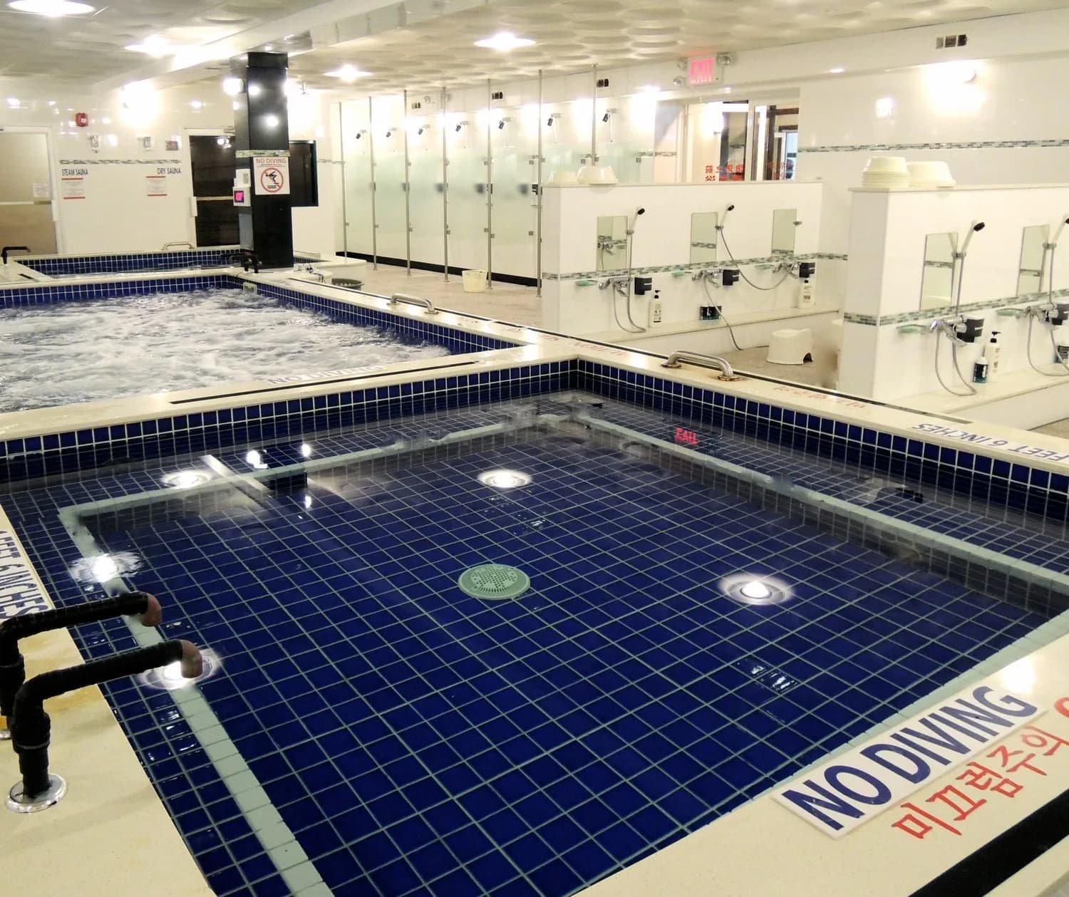 Indoor spa facility with blue-tiled swimming pools, changing stalls, and bright lighting