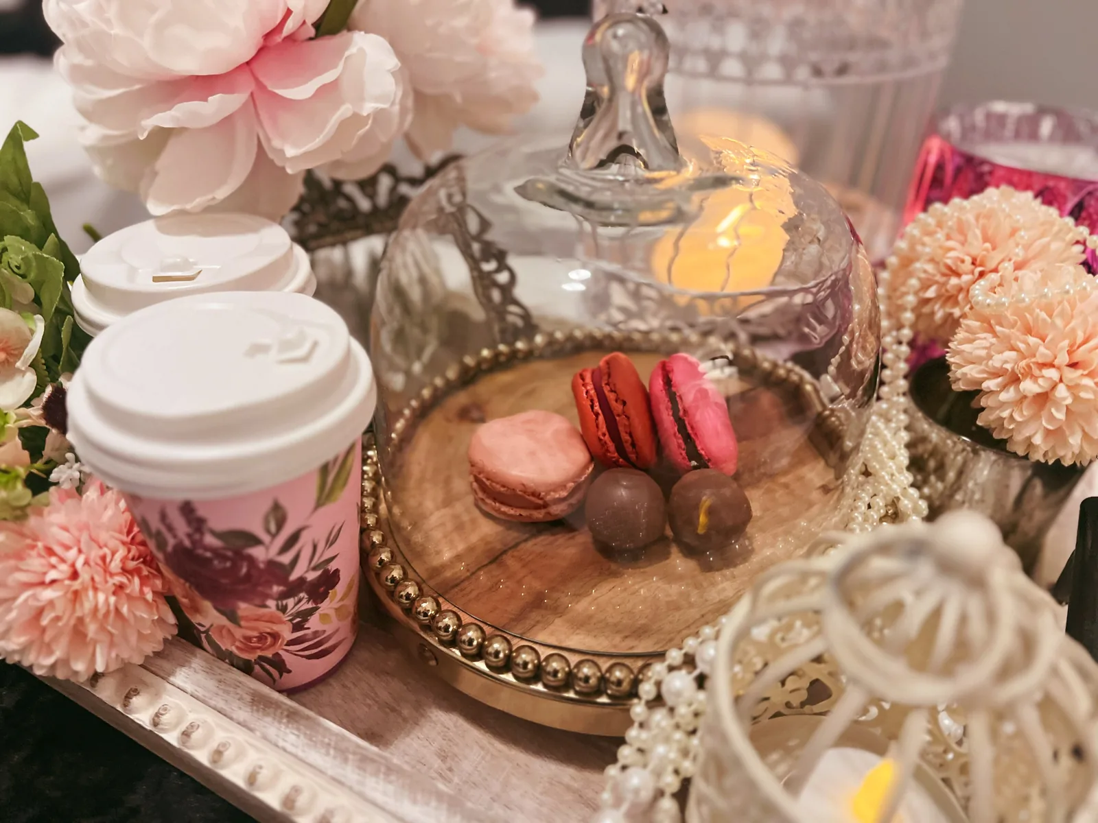Macarons and spa products displayed with pink and white flowers, pearls, and decorative dome.