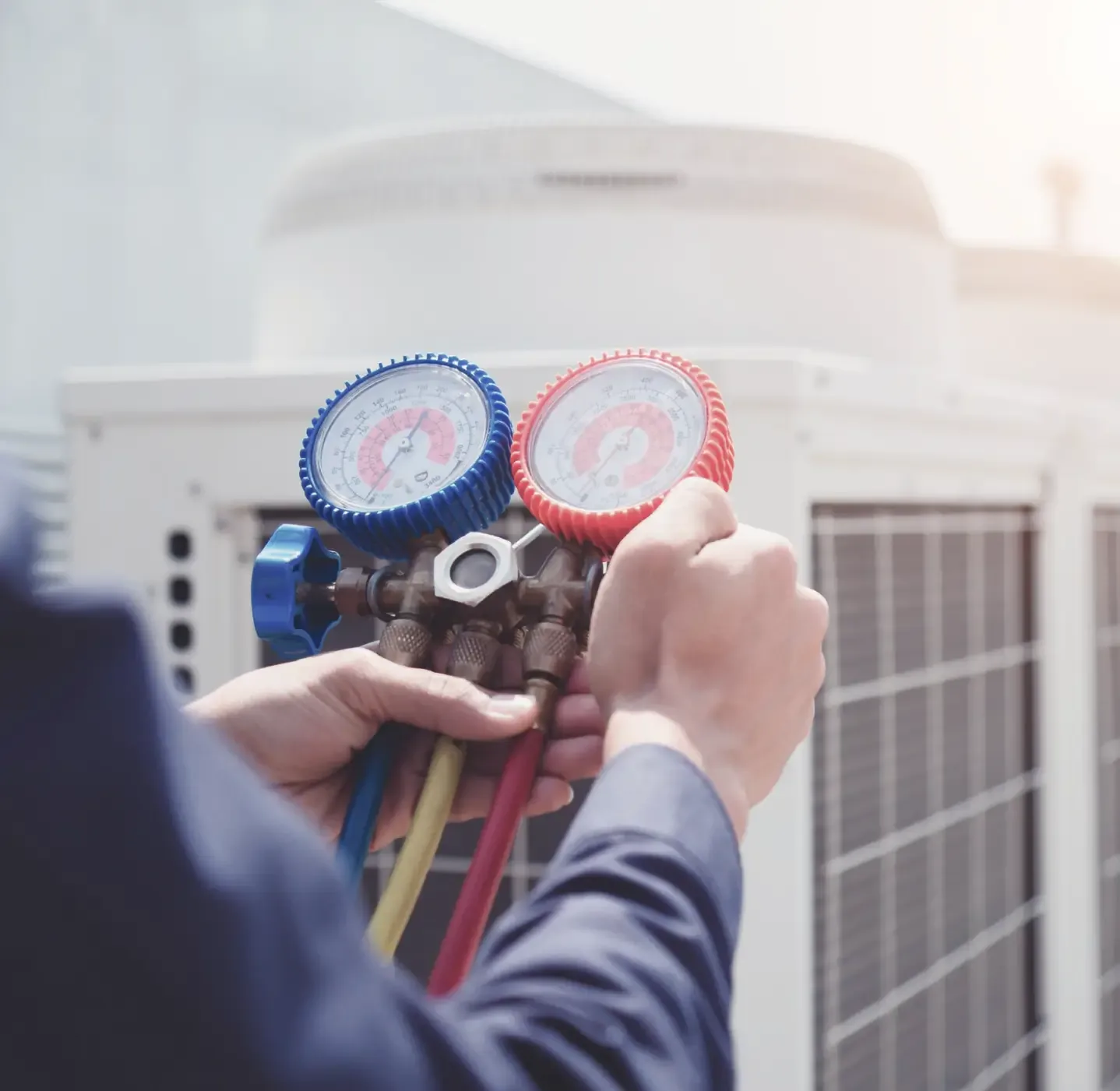 Technician holding refrigerant manifold gauges during AC service, with outdoor unit in background