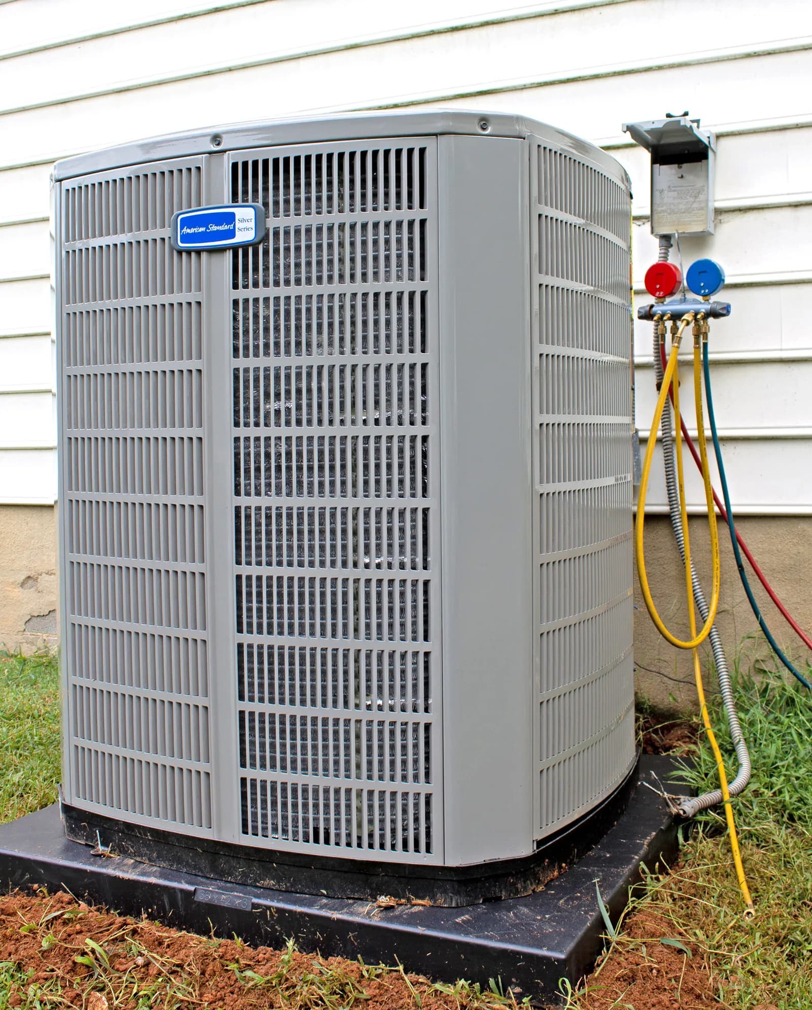 American Standard AC condenser unit with service gauges and hoses attached to exterior of house