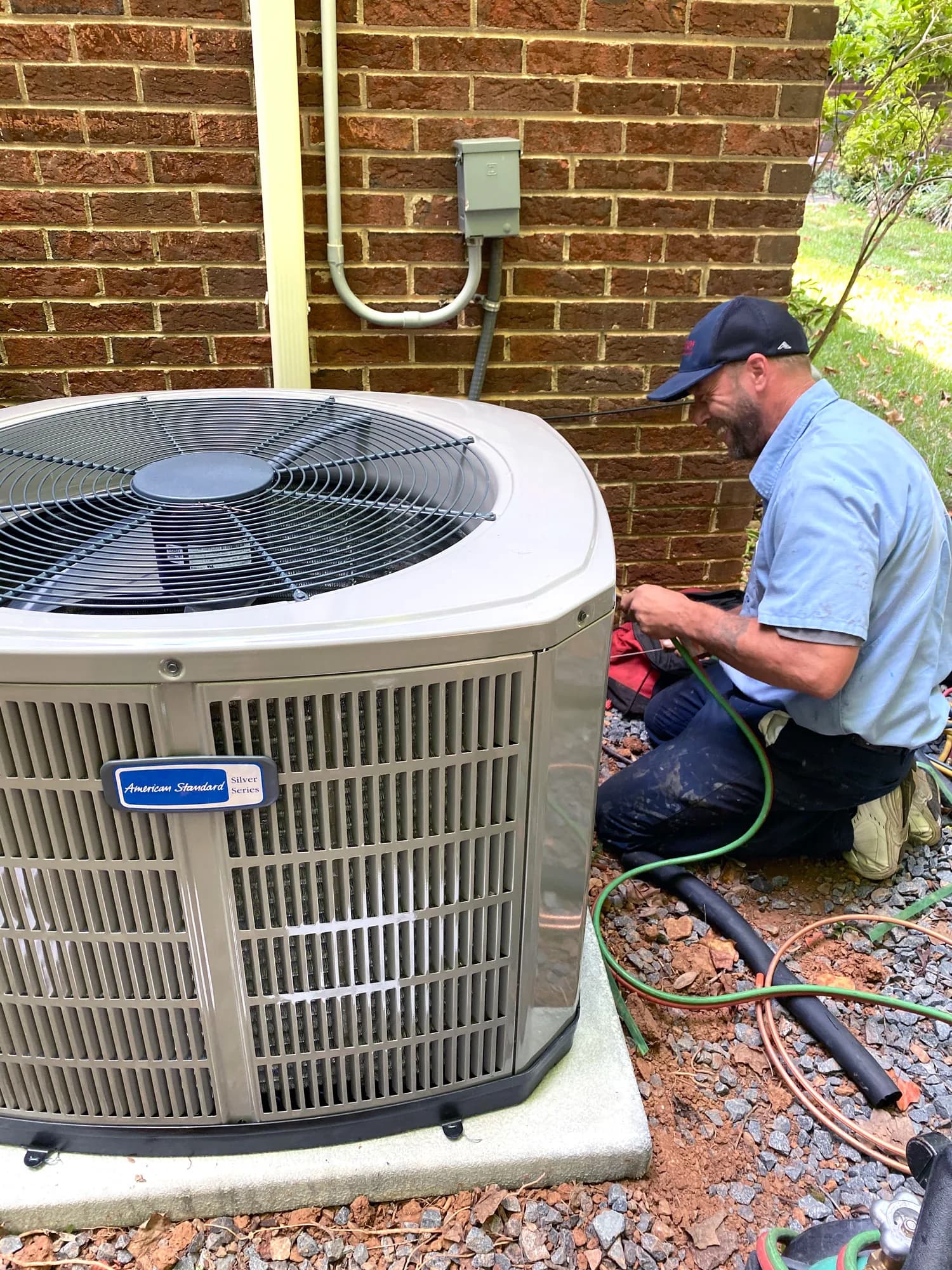 HVAC technician servicing an outdoor air conditioning unit against a brick wall
