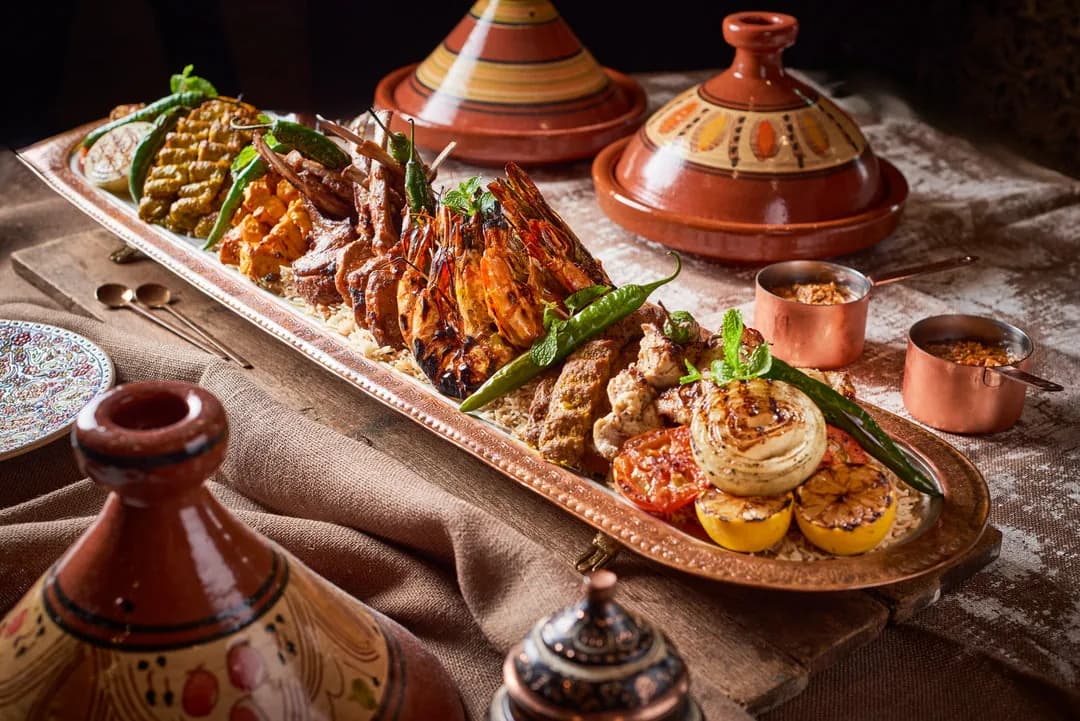 Moroccan tagine feast with roasted meats, vegetables, and traditional copper serving dishes on textured table setting