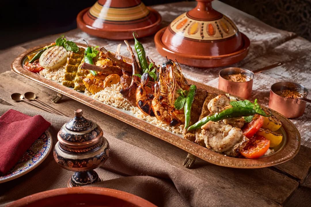 Moroccan tagine with prawns, vegetables, and couscous on wooden platter with clay tagine pots