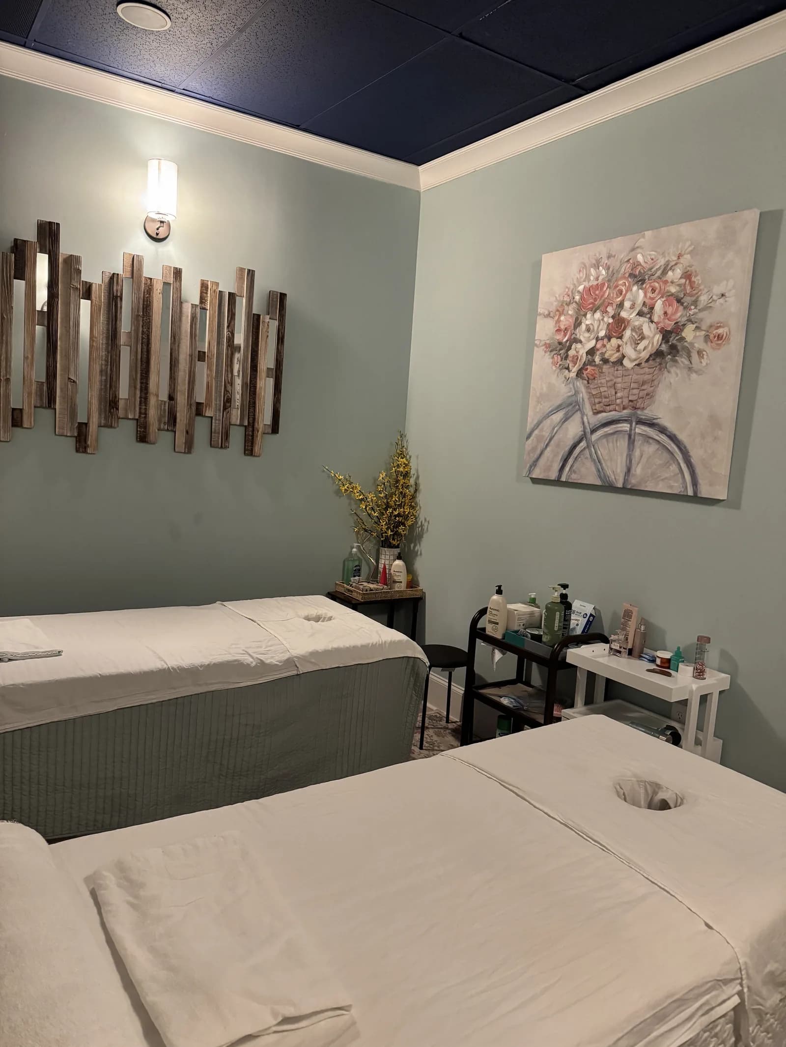 Spa treatment room with massage tables, sage walls, and decorative art