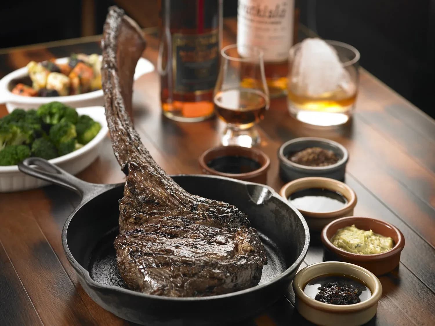 Seared steak being lifted from a hot cast-iron skillet with condiments and drinks on the table