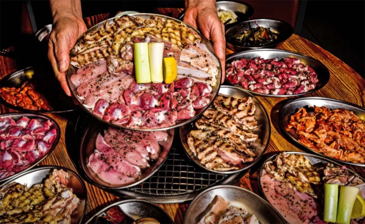Chef holding platter of Korean grilled meats and vegetables with side dishes