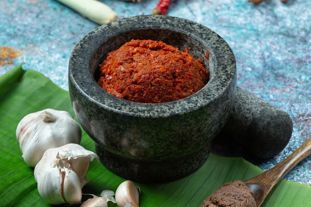 Stone mortar with red chili paste, garlic, and spices on banana leaf