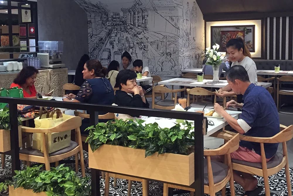 Restaurant interior with diners at tables, attentive server, wooden furniture, and artistic wall mural
