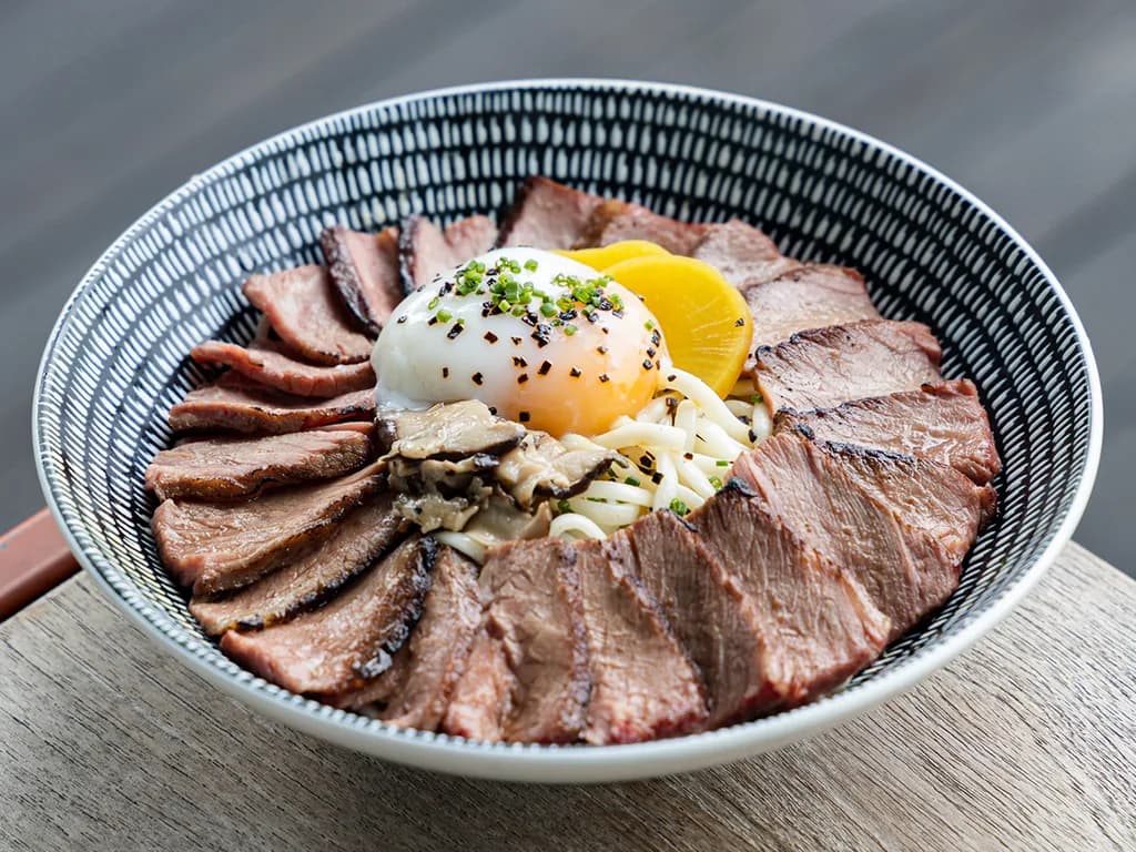 Sliced beef bowl topped with soft egg yolk, green onions, and sesame seeds