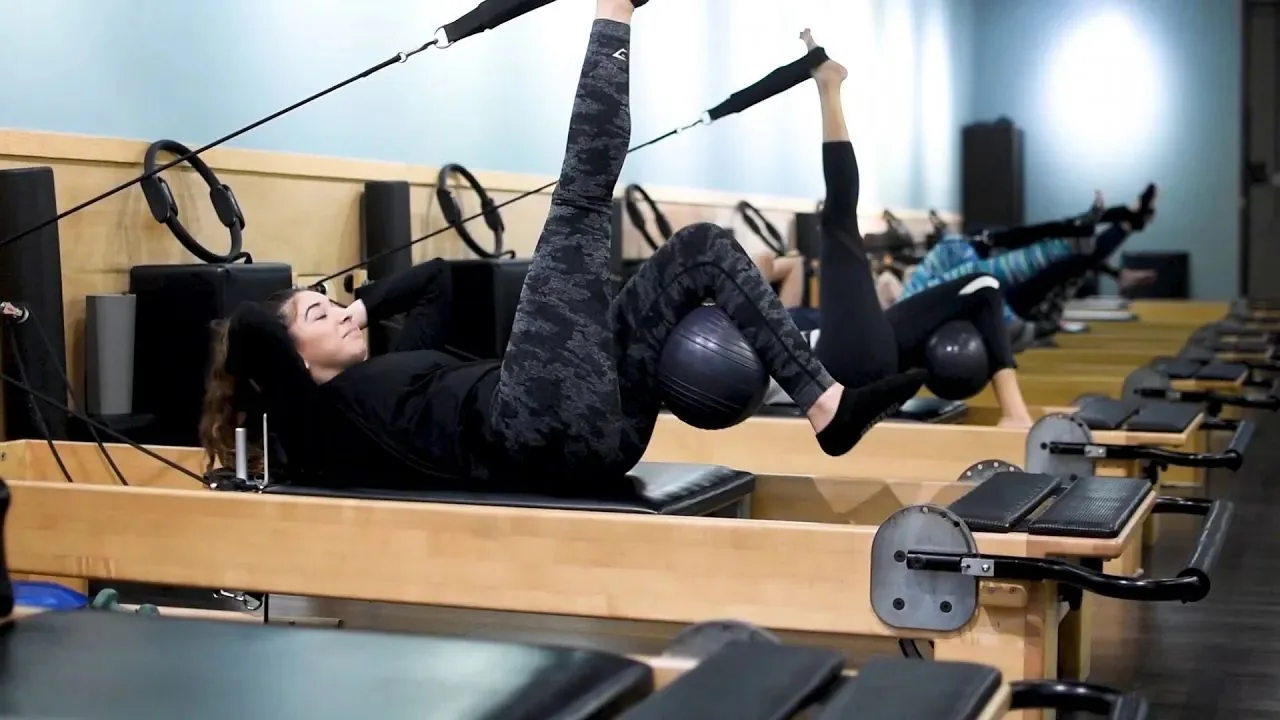 Person doing suspended TRX training exercise in a bright fitness studio with equipment in background.