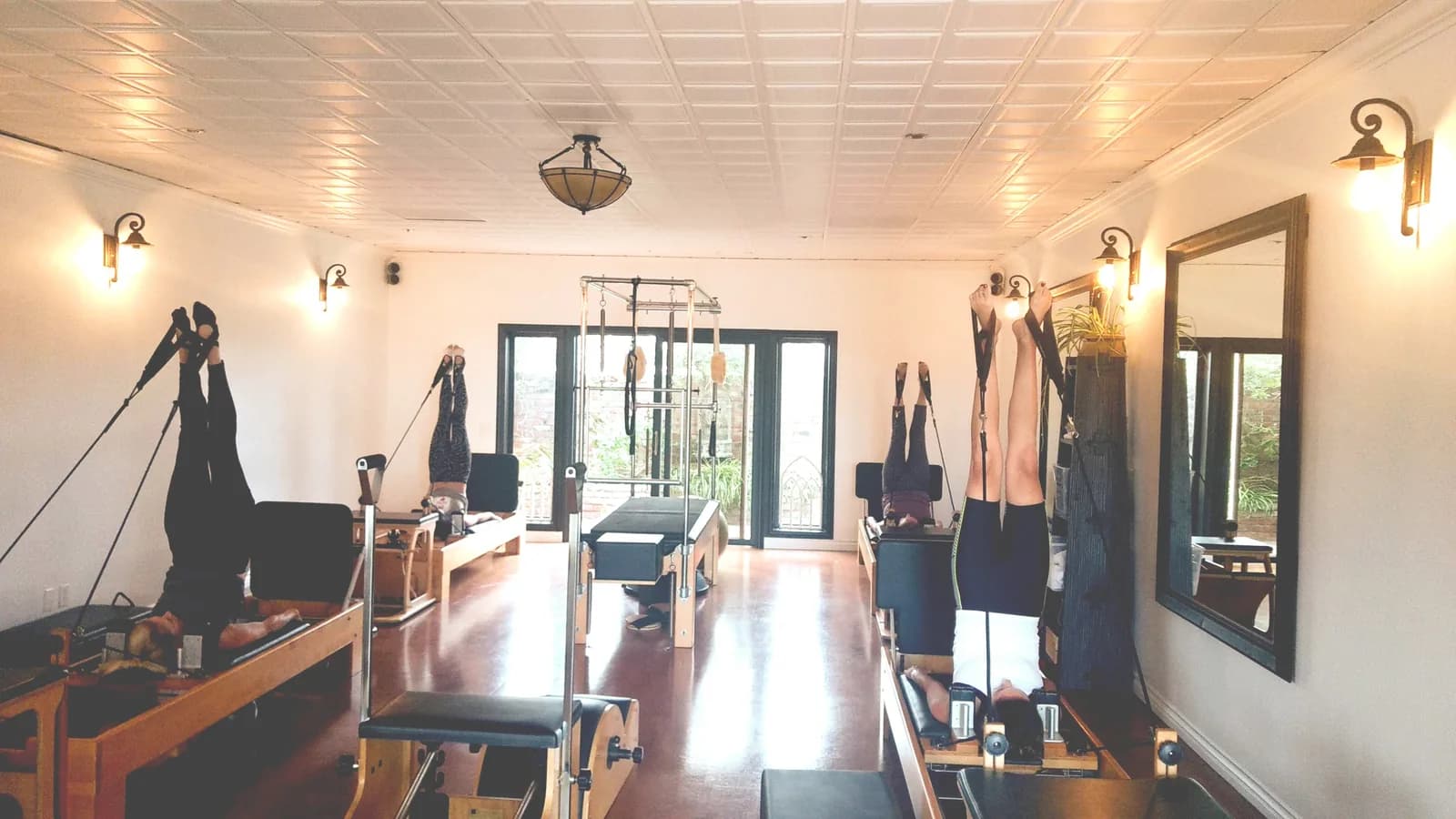 Pilates studio with reformer machines, mirrors, and blonde wood flooring