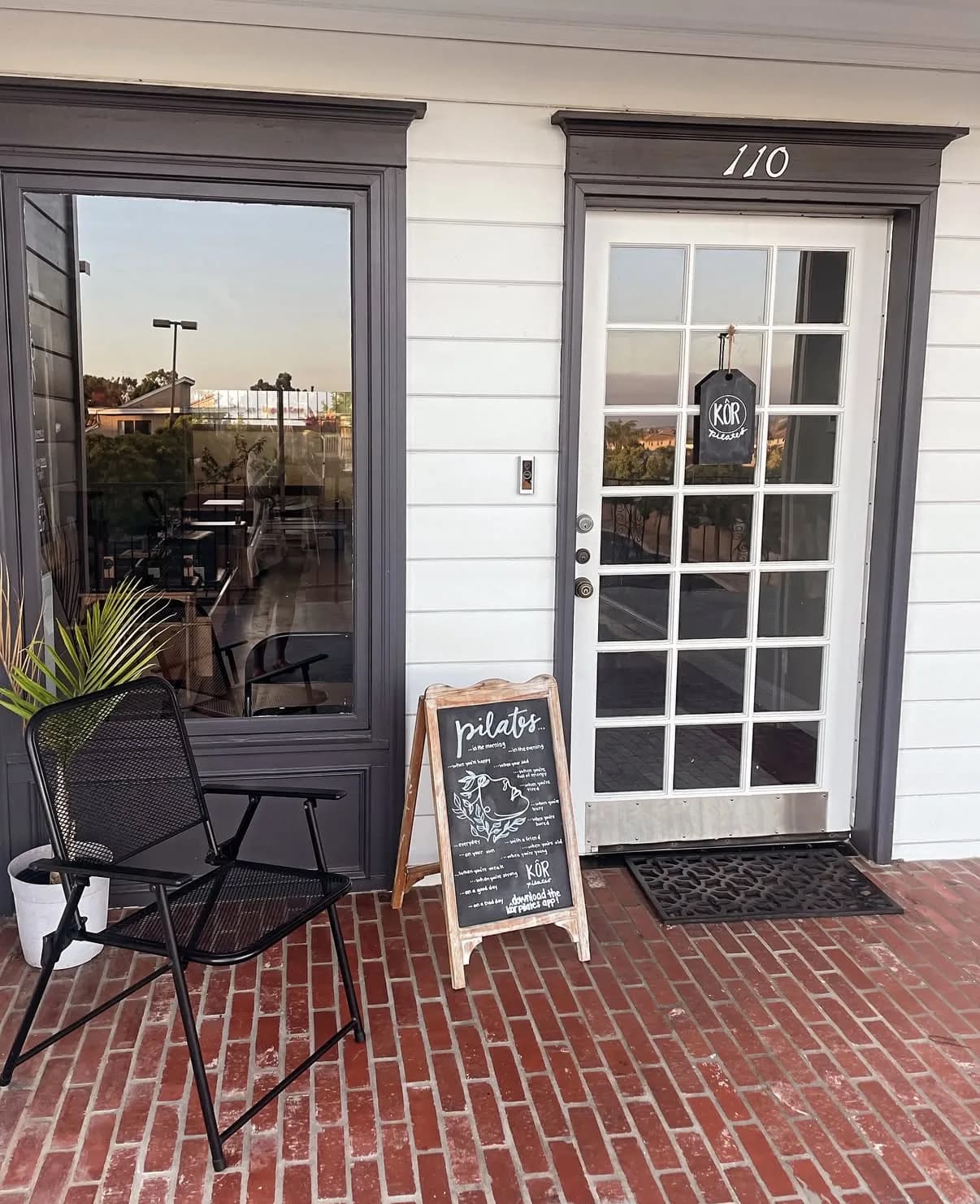 KÔR Pilates storefront with glass doors, outdoor chair, and menu board on brick patio