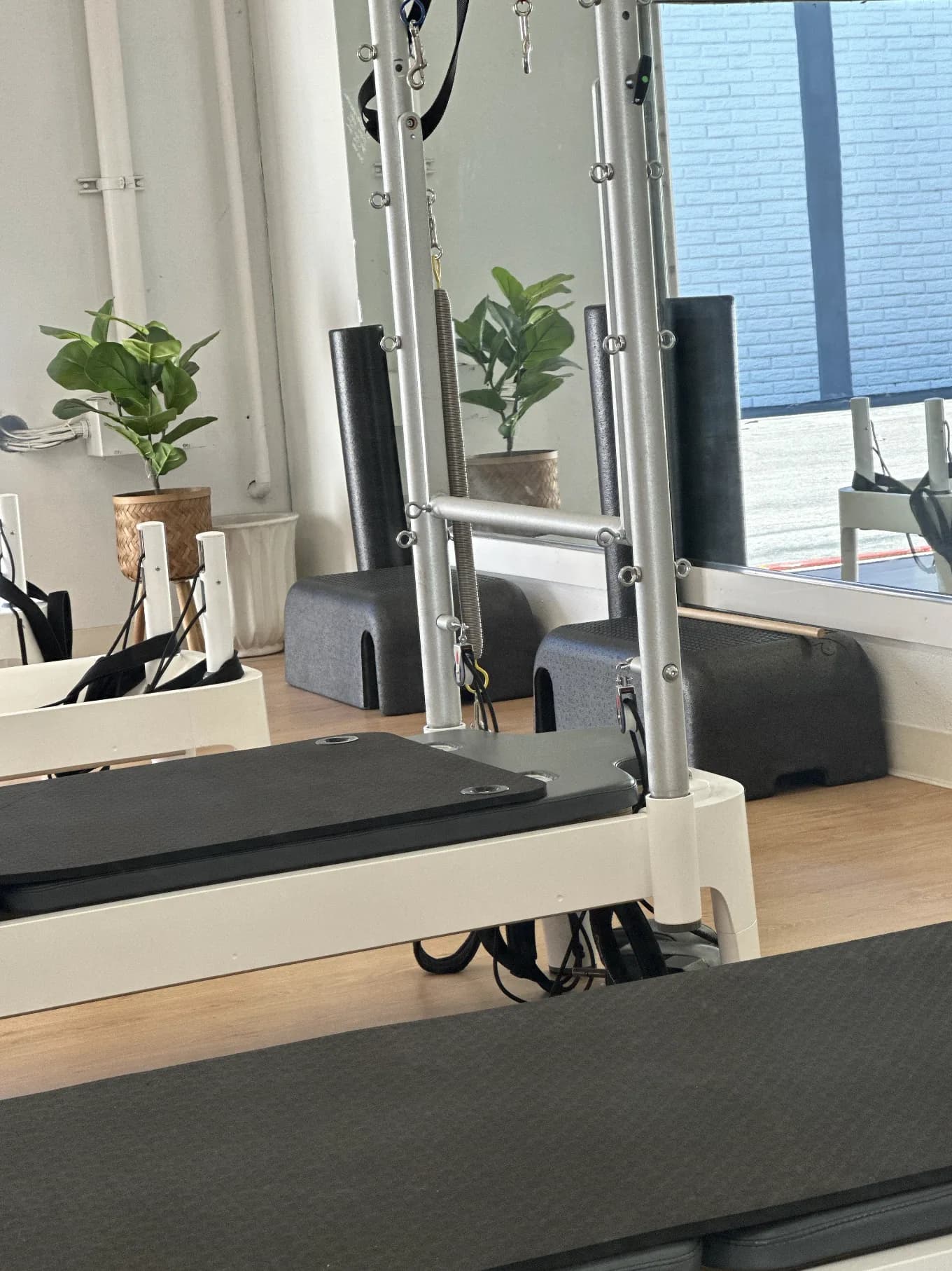Pilates reformer machines in a light-filled studio with plants and large windows