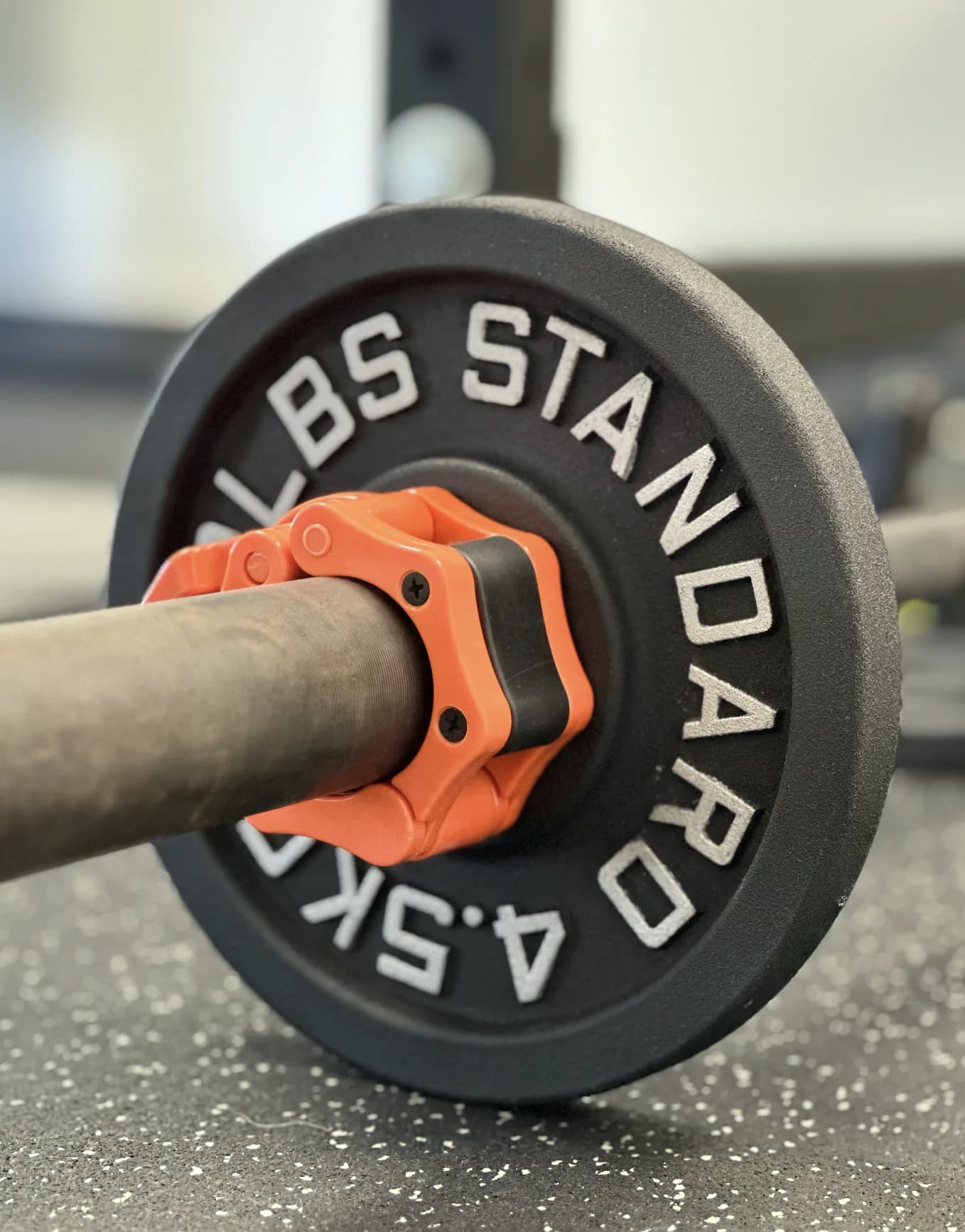 Barbell with 45-pound plate and orange grip collar on gym flooring